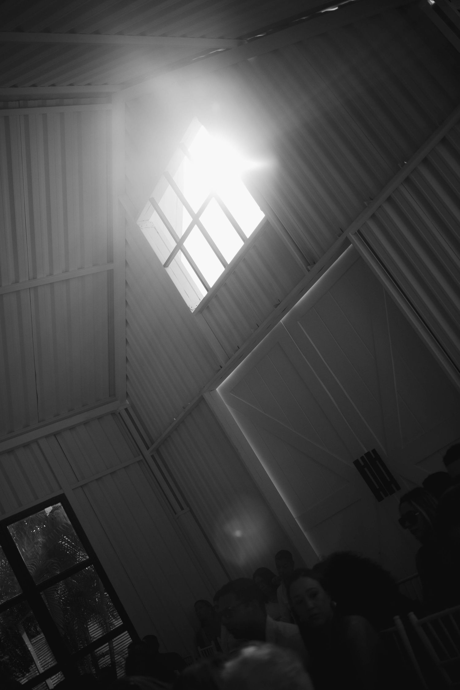 Dramatic sunlight streams through skylights in a dark warehouse ceiling creating striking diagonal beams of light.