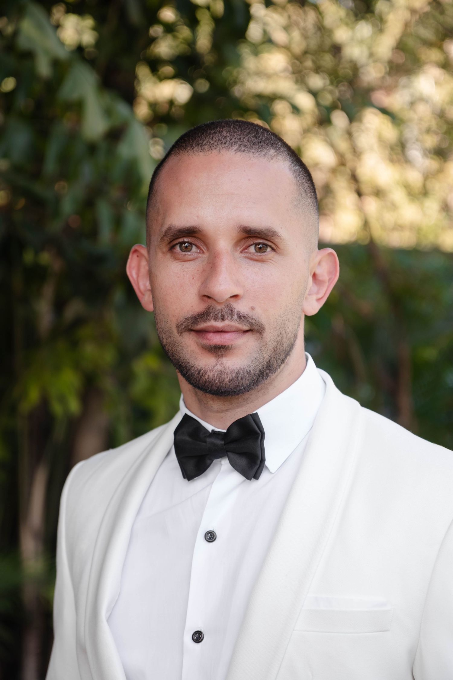 A series of close-up portraits of someone wearing a white tuxedo jacket and black bow tie in an outdoor setting.