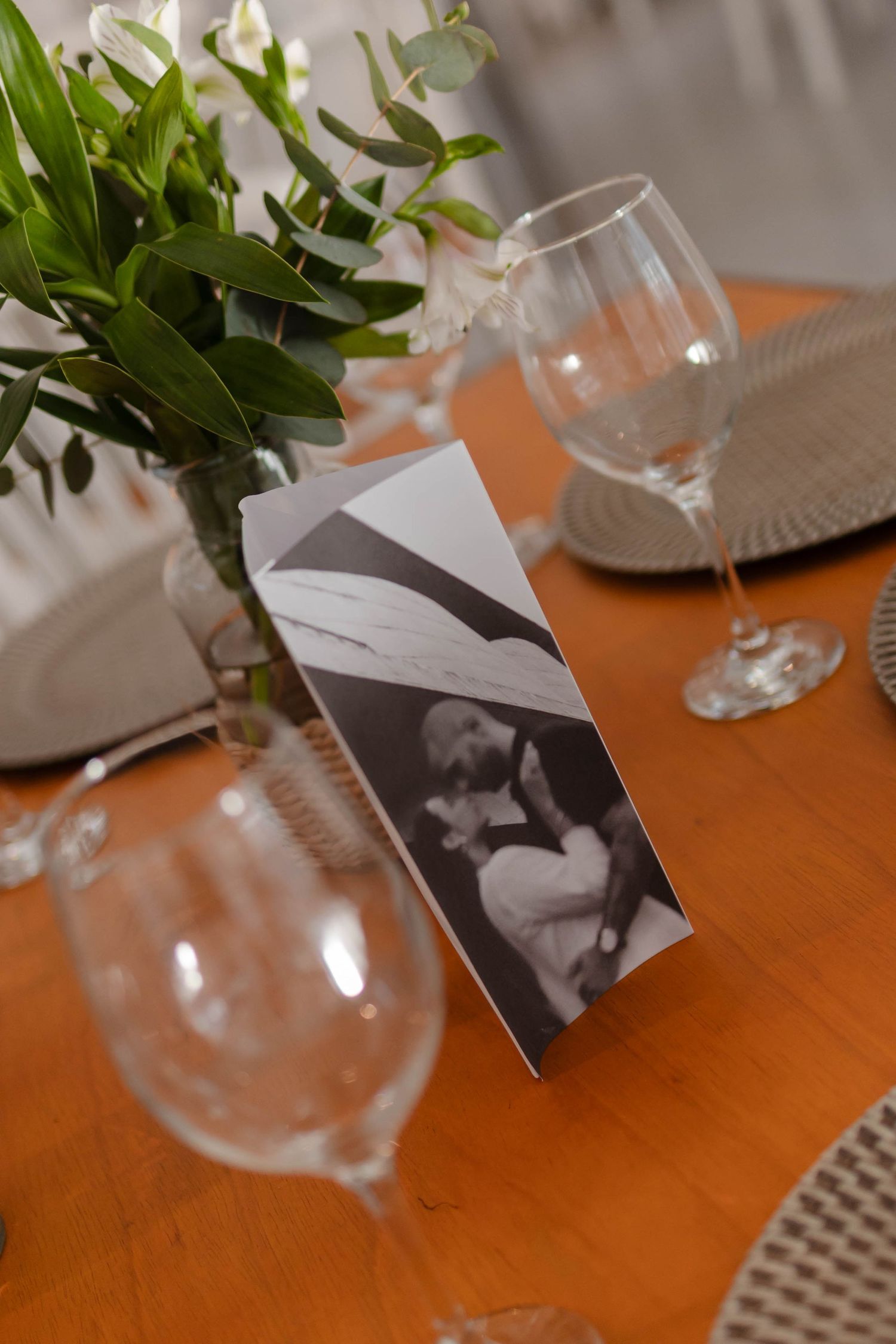 Wine glasses and green plants arranged on a wooden table with black and white photos.