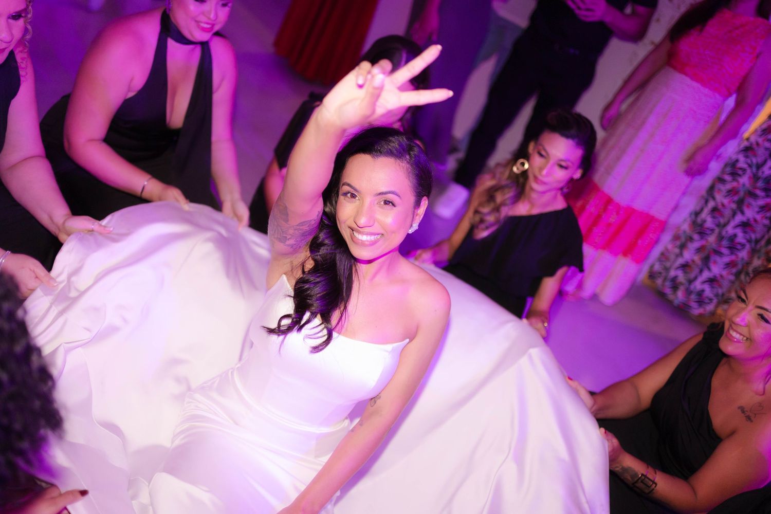 A person in a white wedding dress spins and dances at a reception under purple lighting.