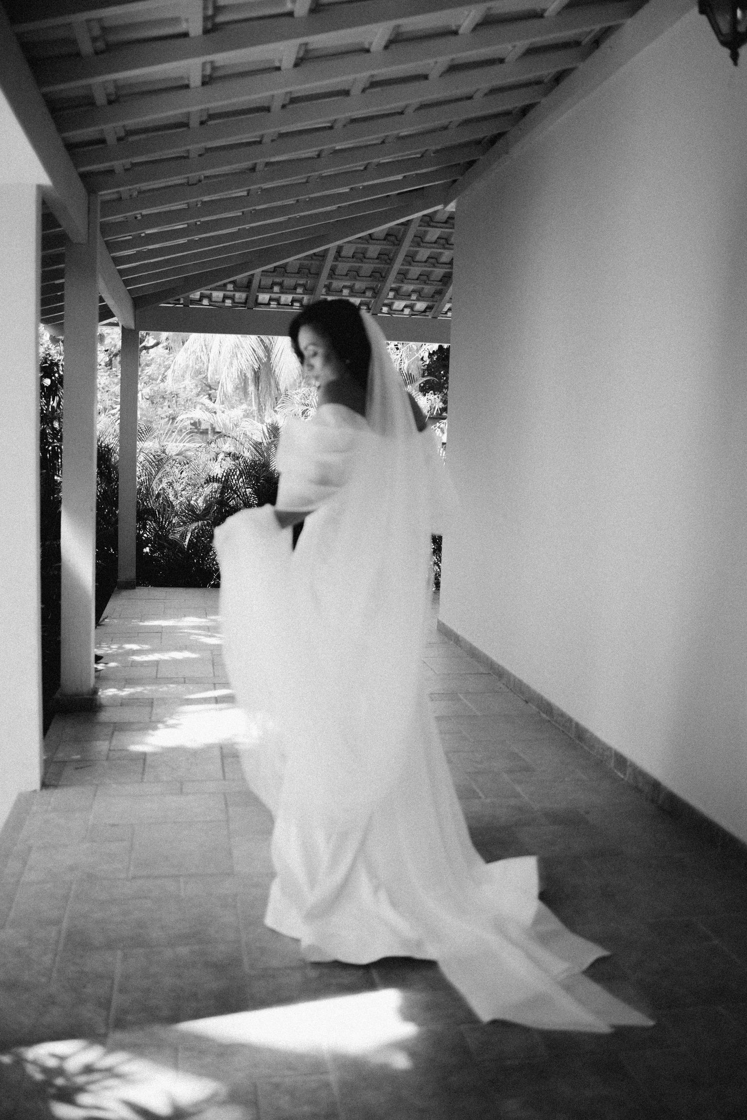 Flowing white wedding dress movement captured in a covered outdoor walkway.