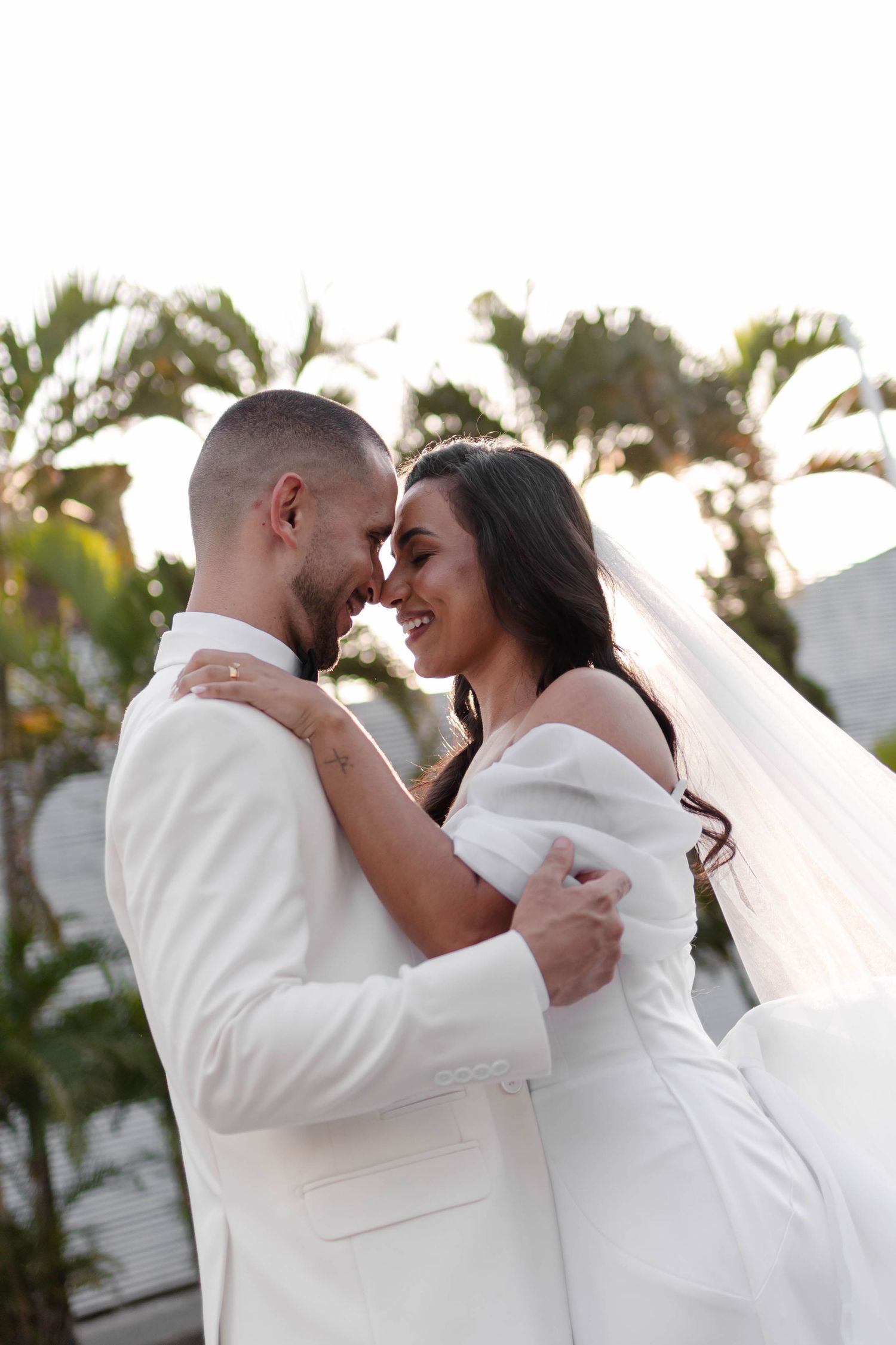 Newlywed couple in white embraces during outdoor wedding photoshoot.