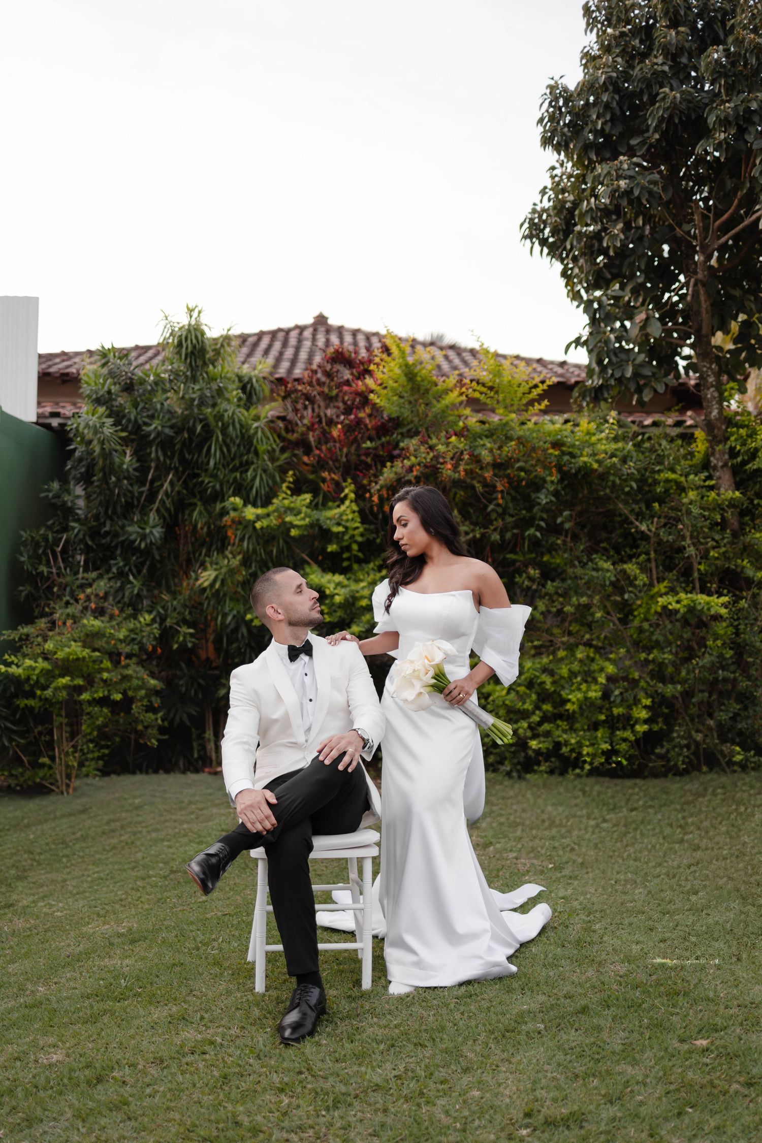 A couple relaxes on outdoor furniture in a garden setting with greenery in the background.