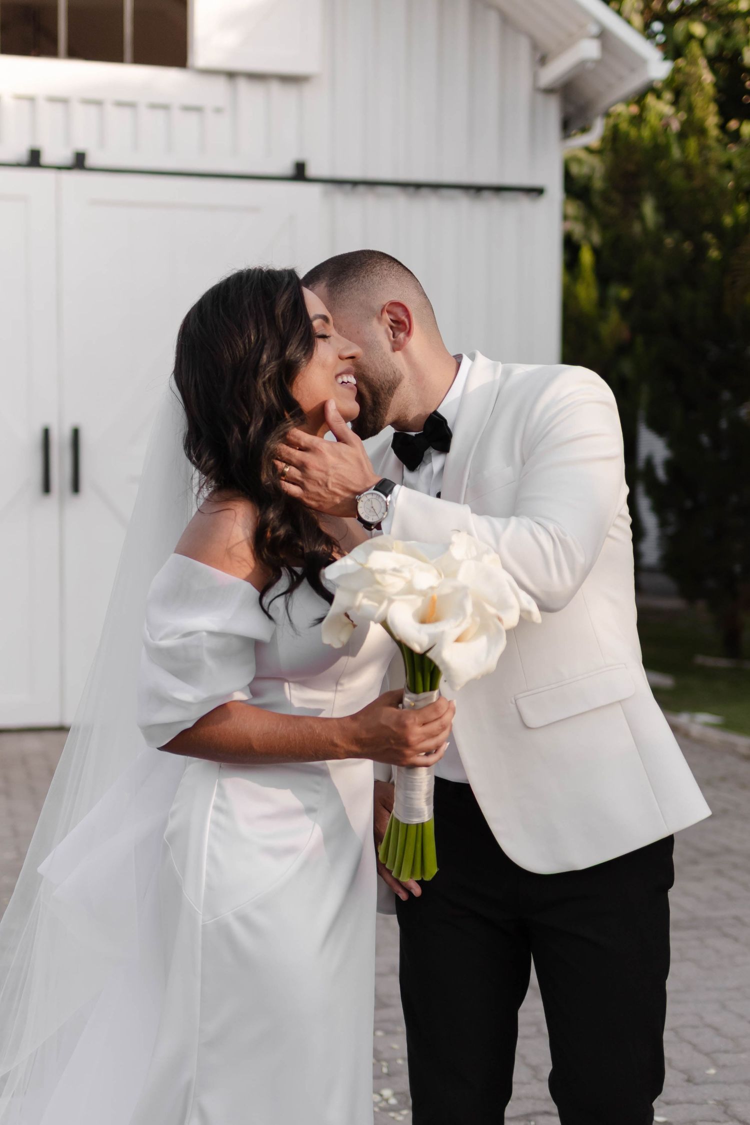 Romantic wedding couple sharing intimate moment with white bouquet outdoors.