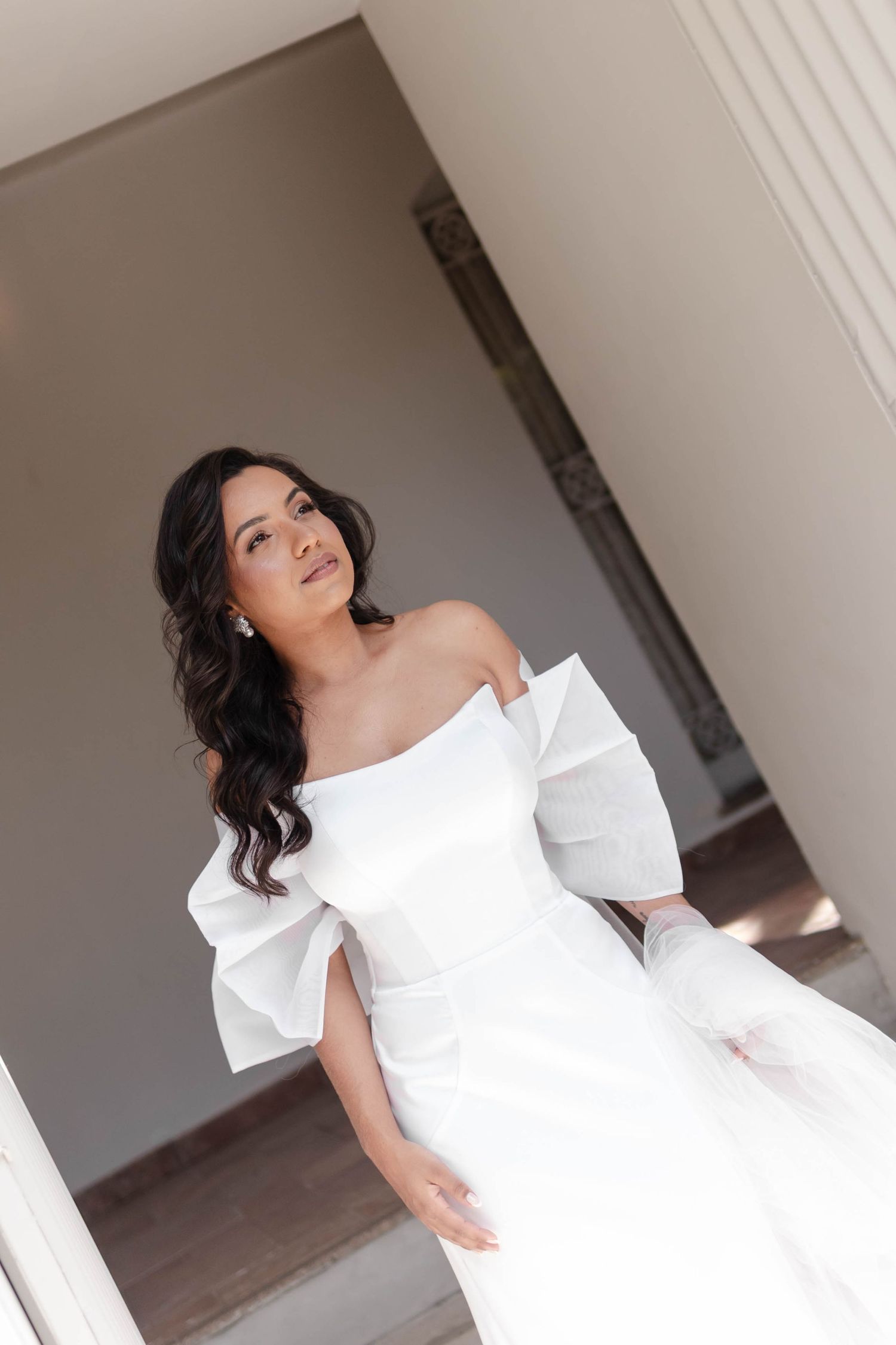 Elegant white off-shoulder wedding dress with puff sleeves and flowing skirt photographed in a minimalist indoor setting.