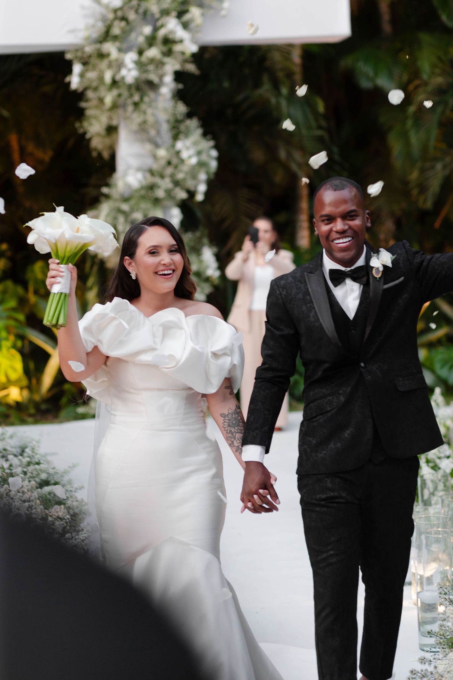 Newlyweds walking together under floral arch during outdoor ceremony.