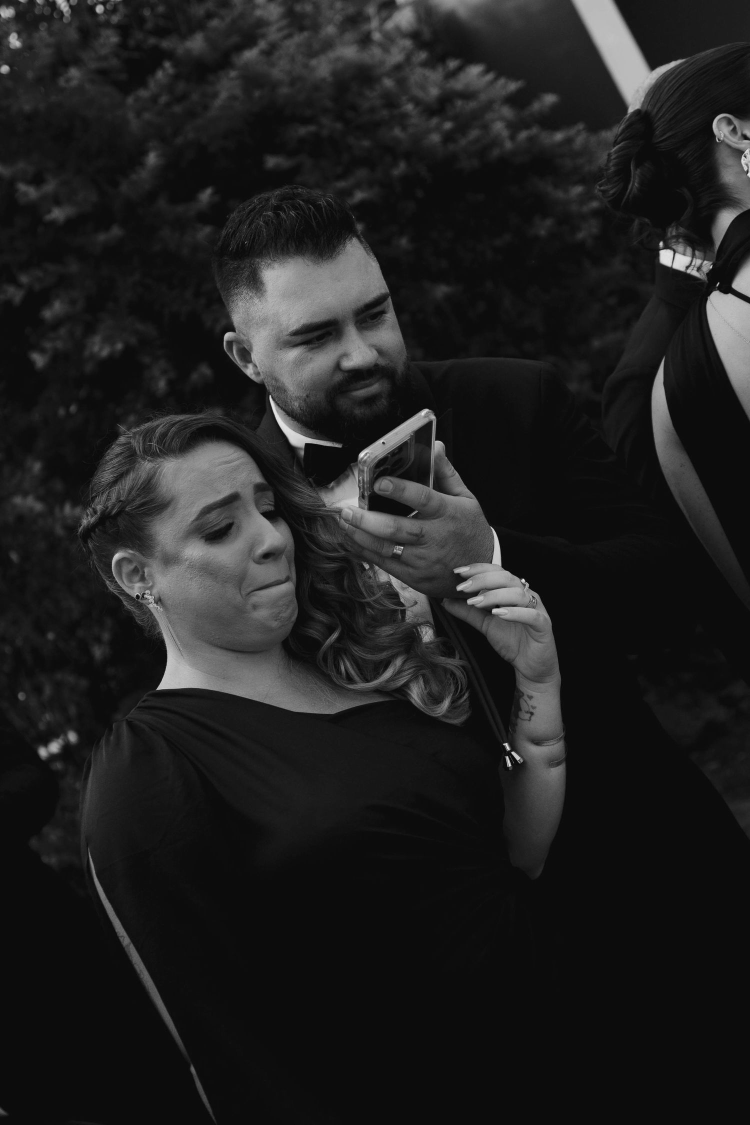 Black and white photo of couple sharing a tender moment outdoors while looking at a mobile phone.