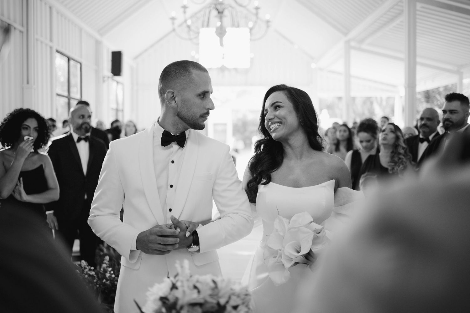 Wedding guests dance and celebrate during an elegant reception in a white tent with crystal chandeliers.
