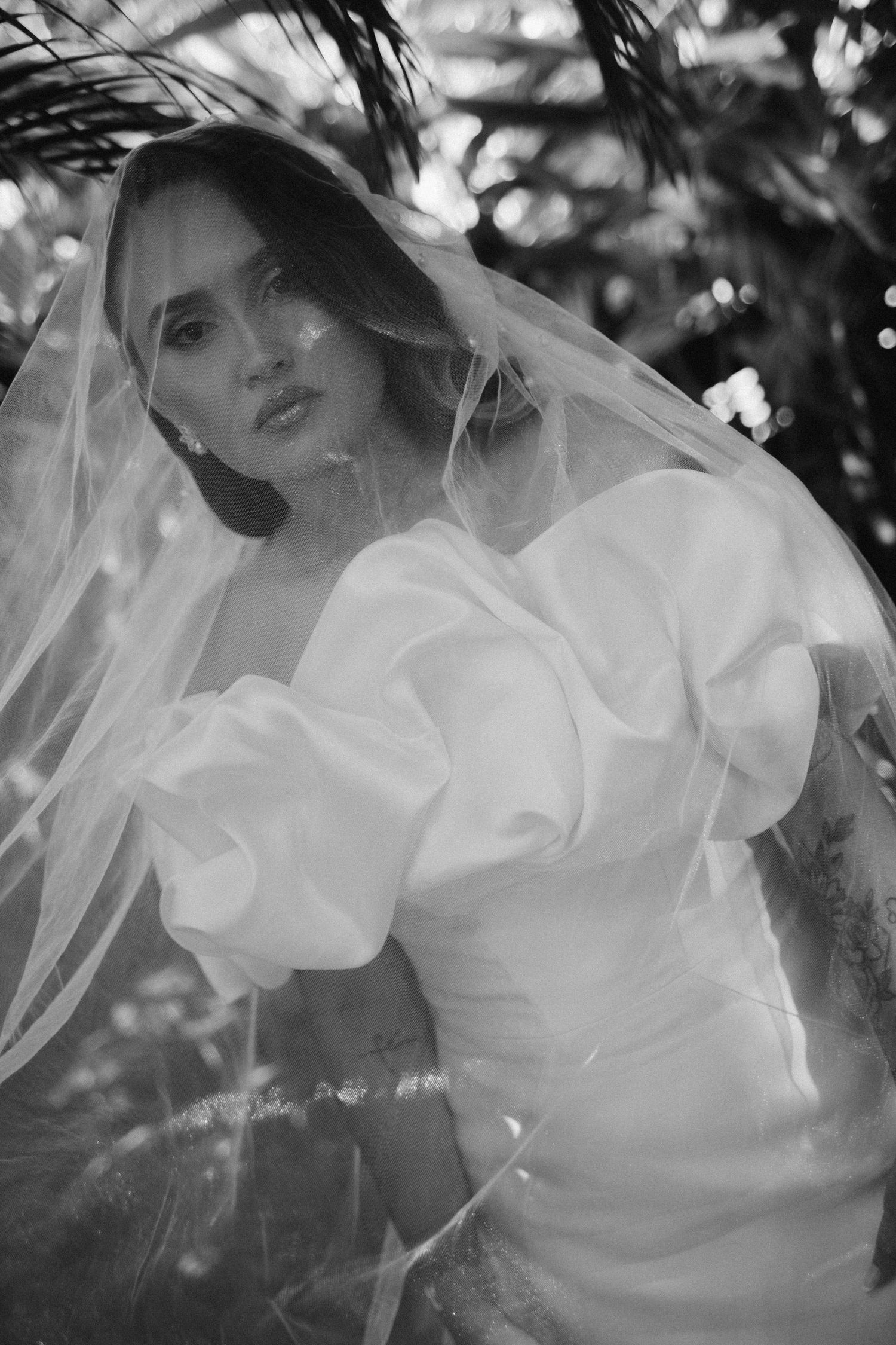 Black and white artistic bridal portrait with flowing veil creating ethereal movement against natural backdrop.