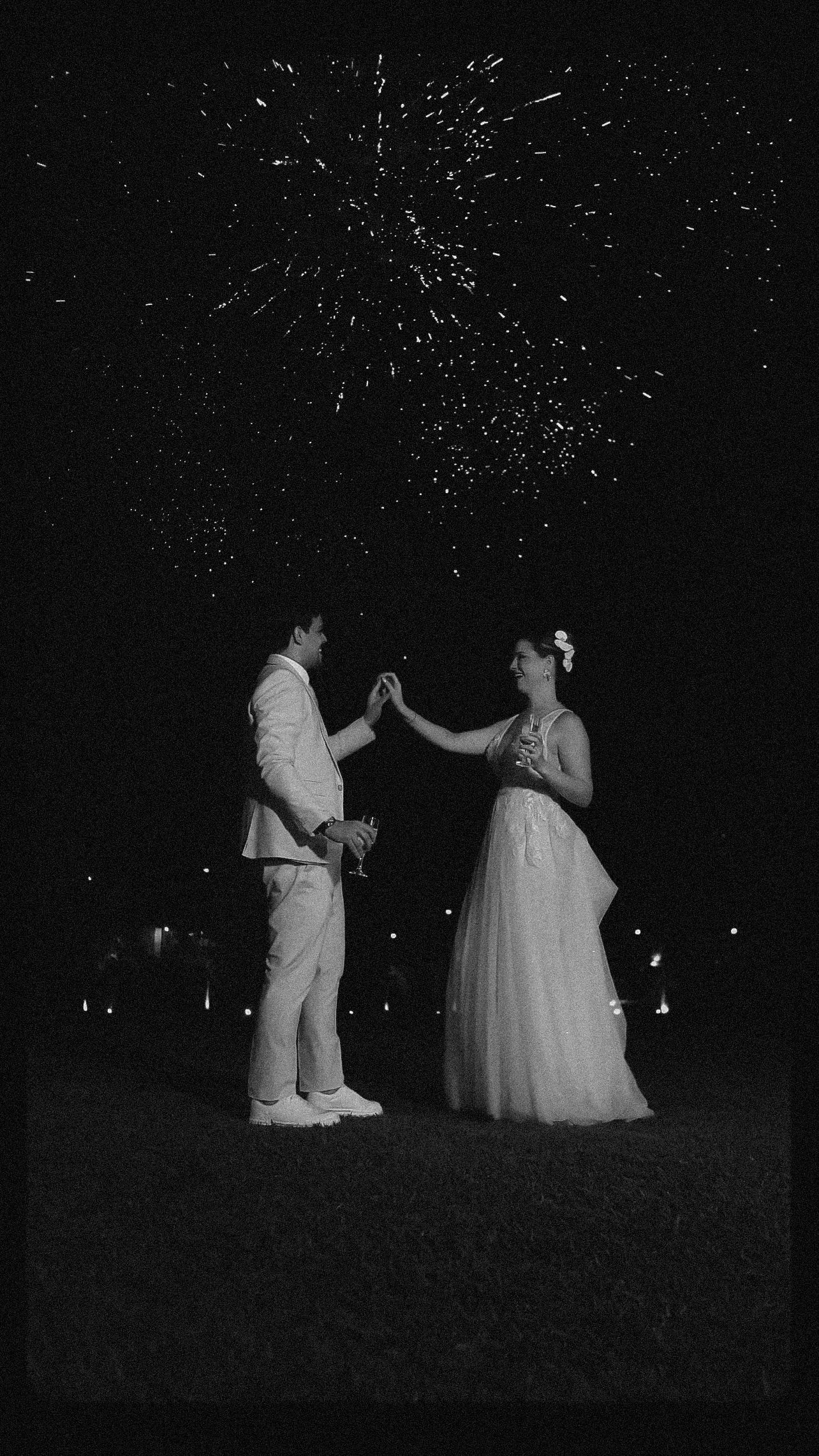 A couple dancing under sparkling fireworks at night in formal wedding attire.