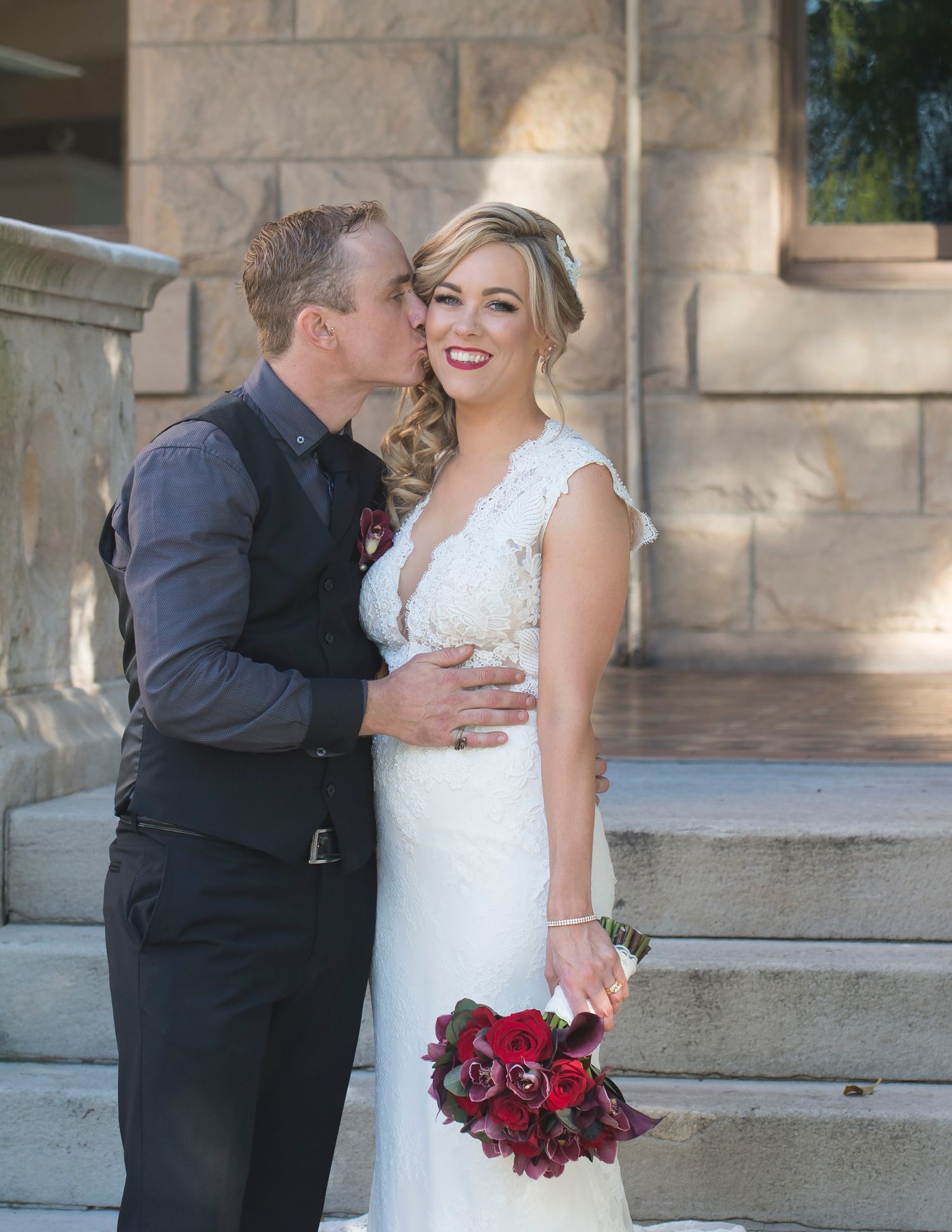 A romantic wedding couple shares tender moments in front of a stone building with elegant archways.