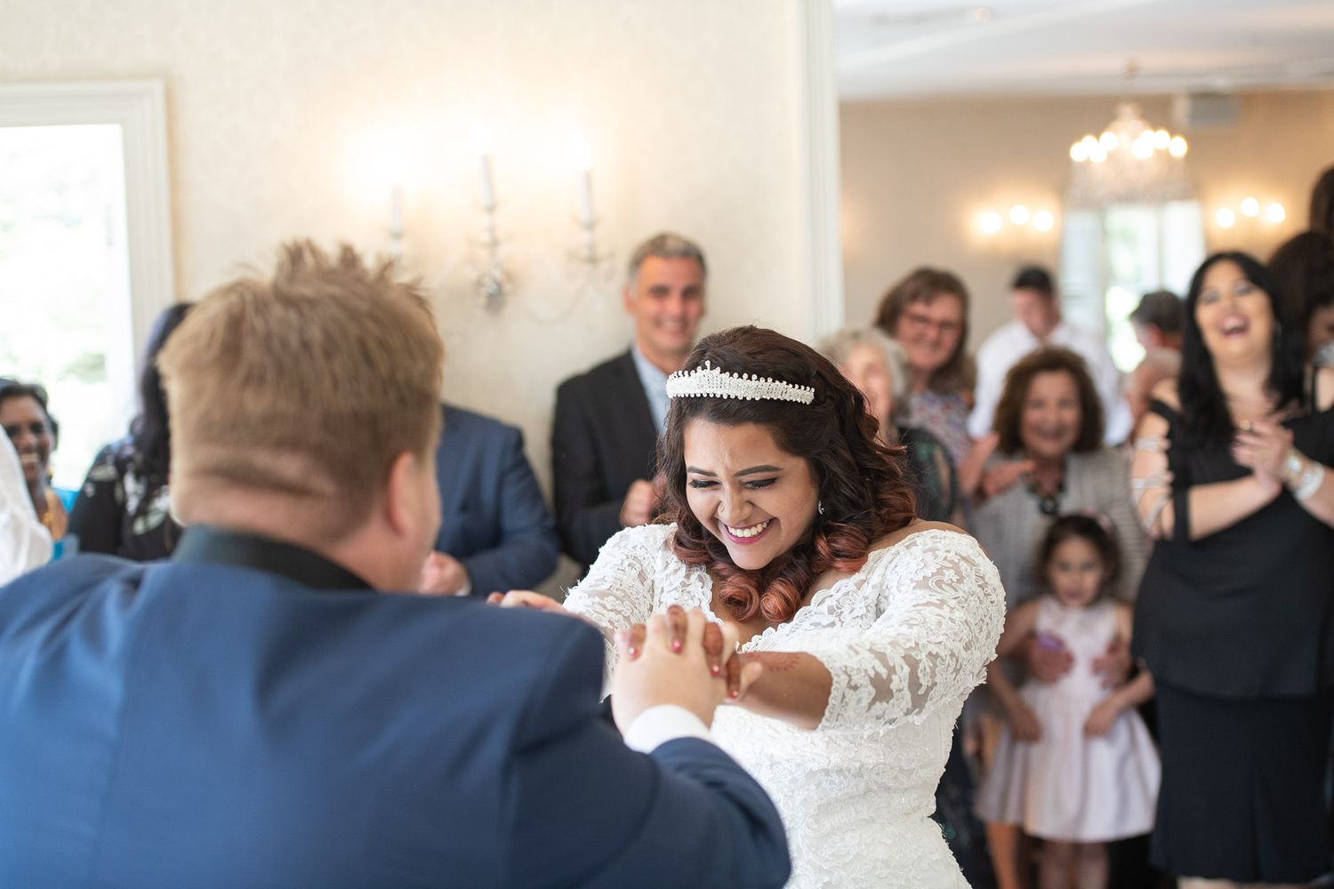 A bride and groom share their first dance at a wedding reception surrounded by guests watching and smiling.
