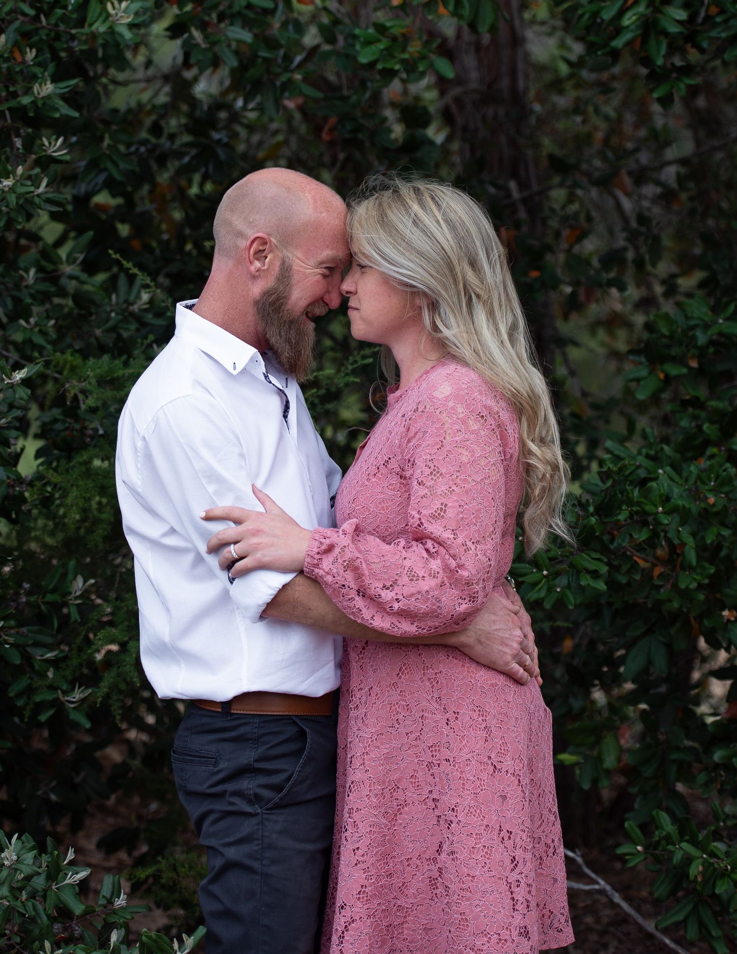 Romantic engagement photos of a couple in pink and white attire against a green backdrop.