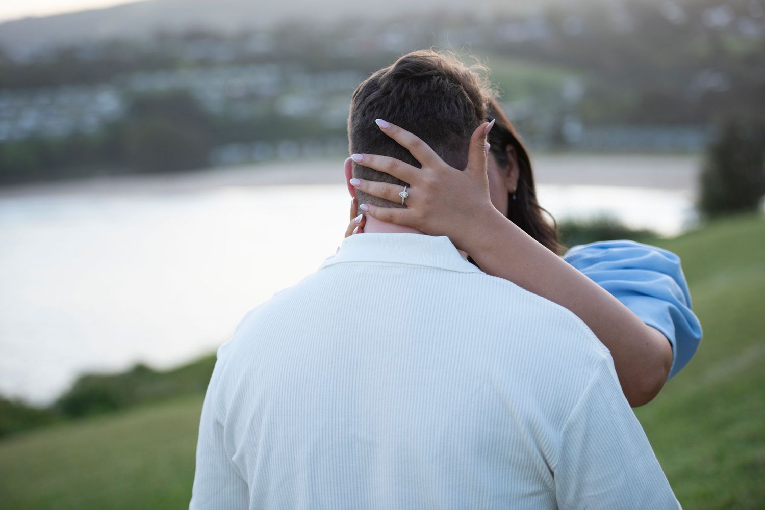 Intimate moment captured between couple on scenic hilltop with water view.