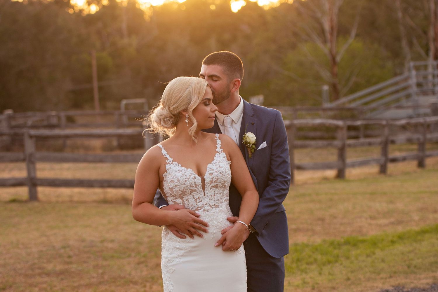 A couple embraces during their wedding photoshoot at sunset in a rustic outdoor setting.