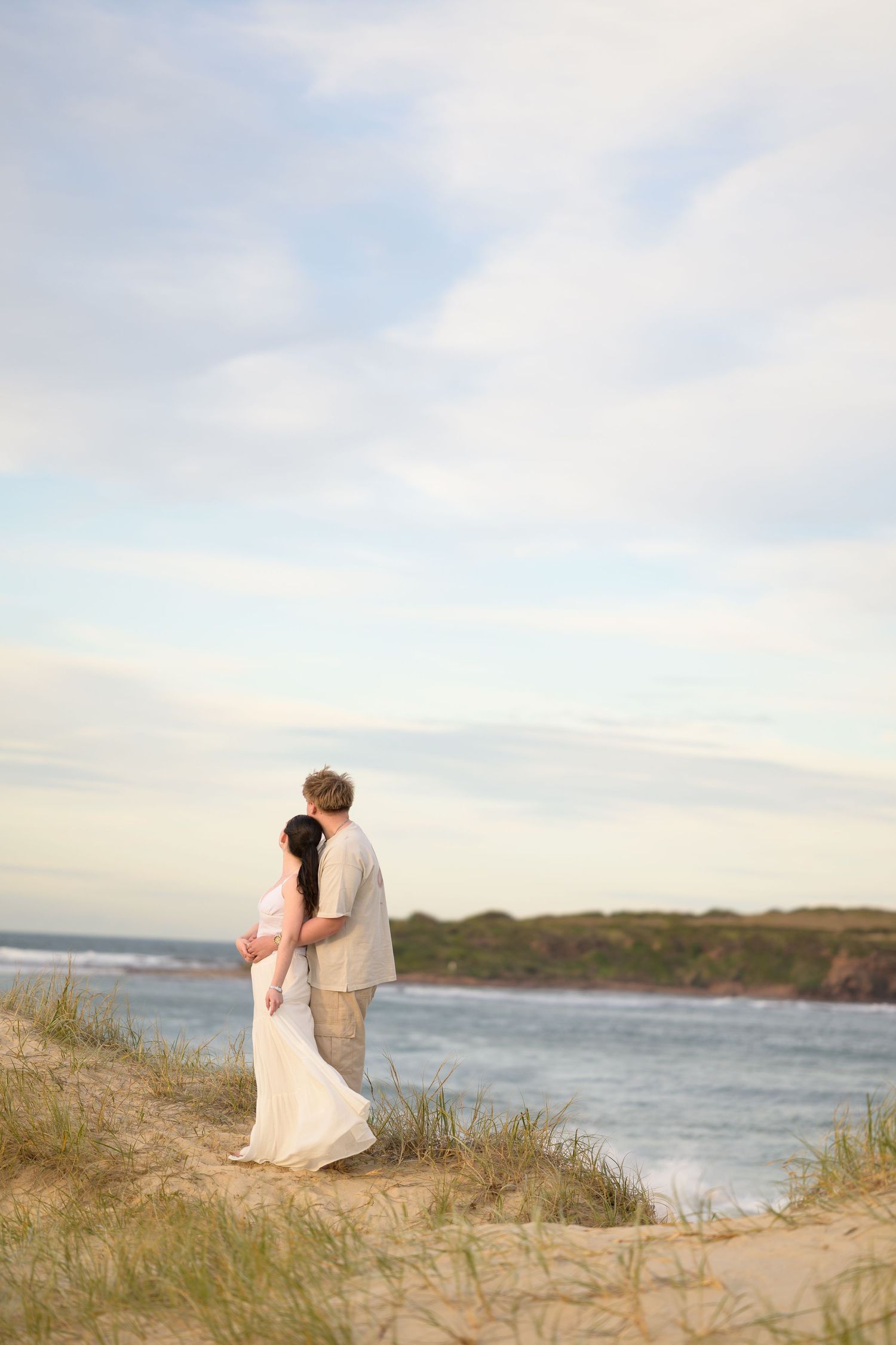 Couple together on coastal sand dunes overlooking ocean at sunset at Warilla beach.