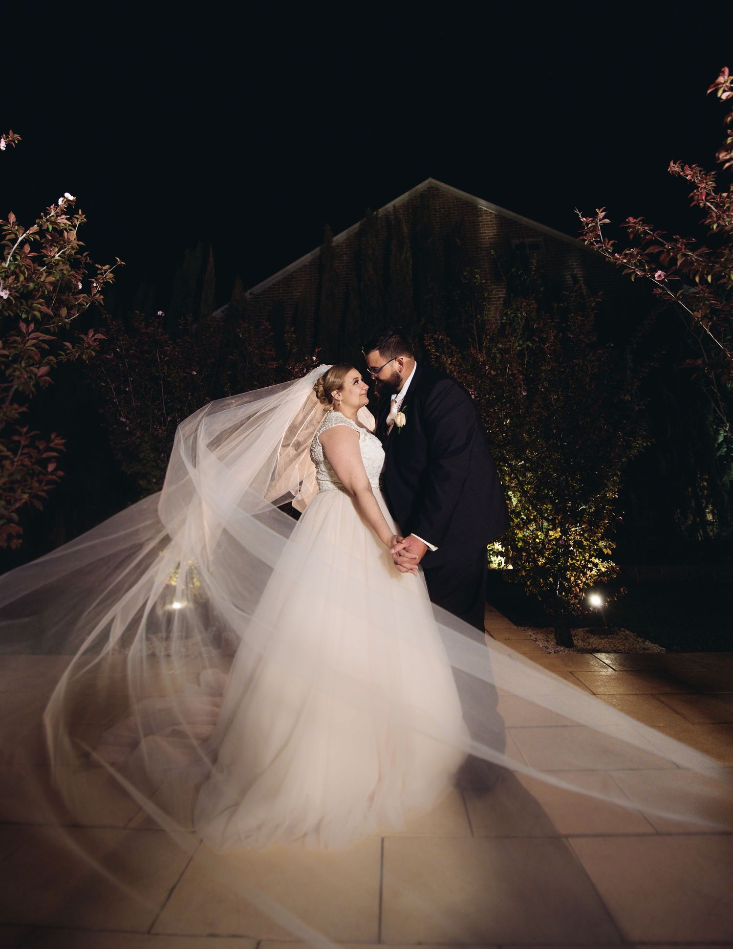 A romantic wedding couple in an elegant dance pose on a moonlit terrace with flowing veil.