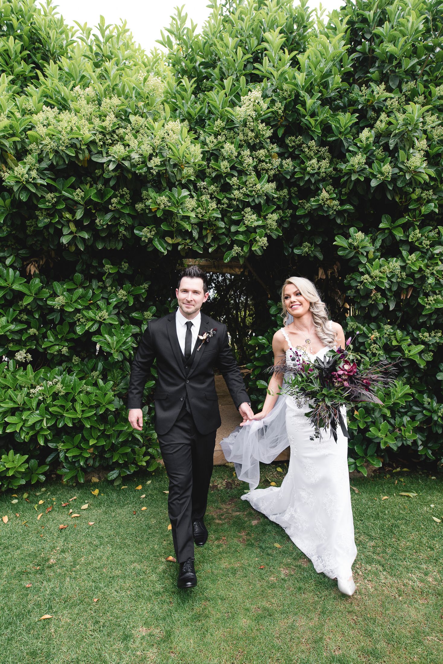 A wedding couple walks through a lush garden setting with green hedges and grass in a sequence of candid moments.