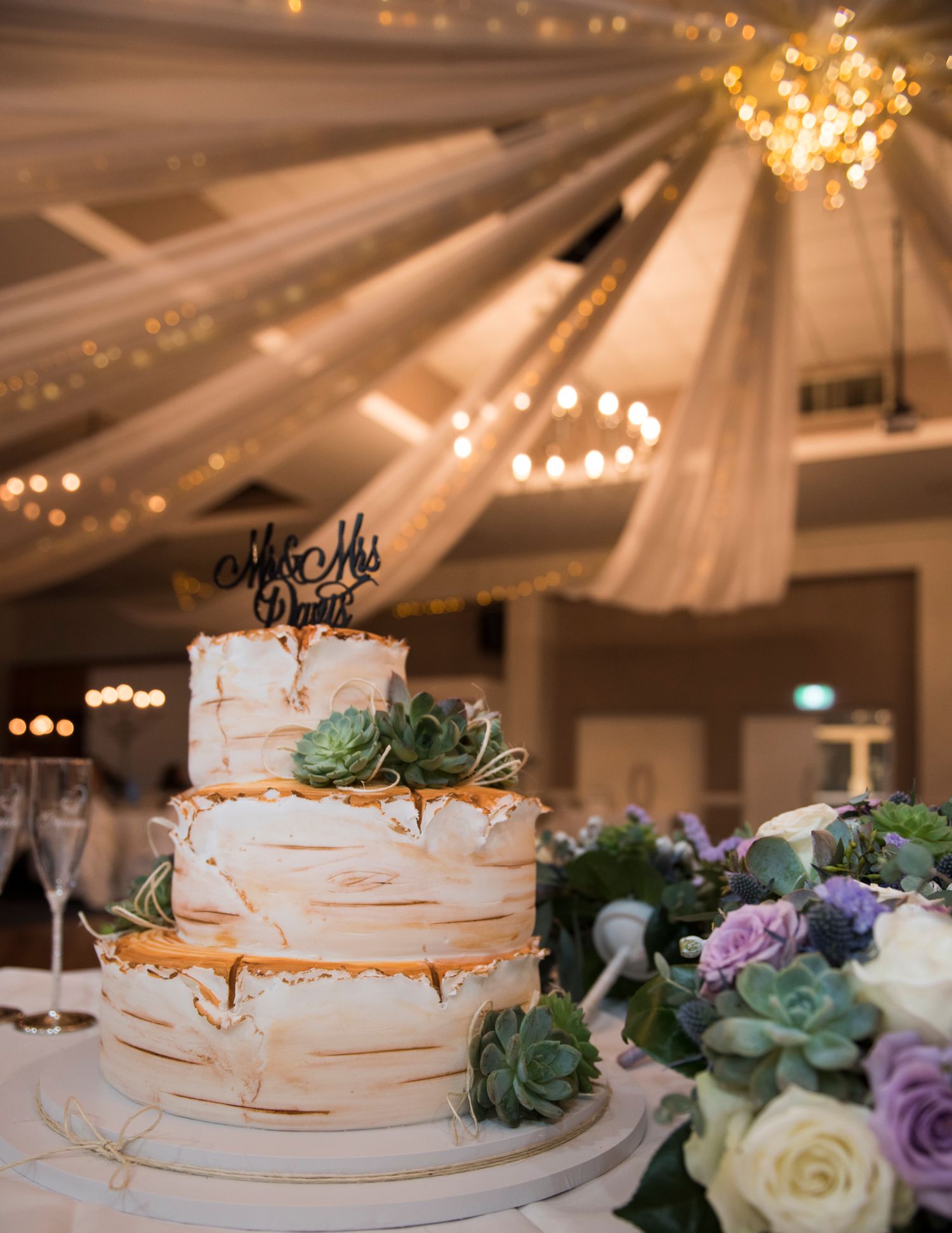 Elegant three-tier white wedding cake decorated with succulents and gold accents.