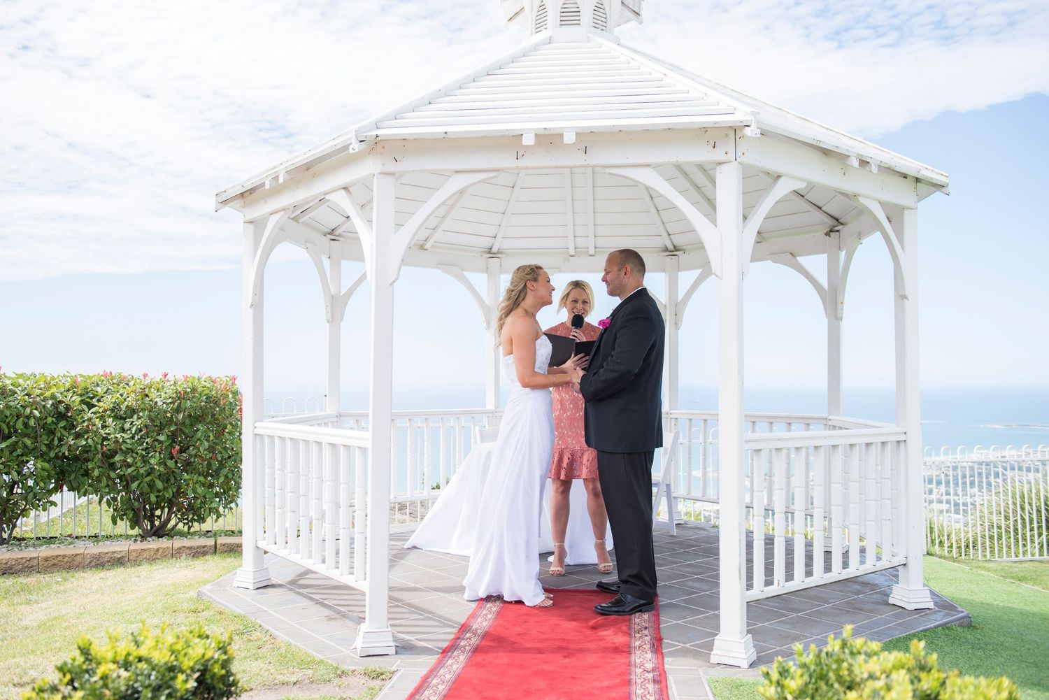 Bride and groom during ceremony under an elegant white gazebo overlooking the ocean on a sunny day at Panorama House.