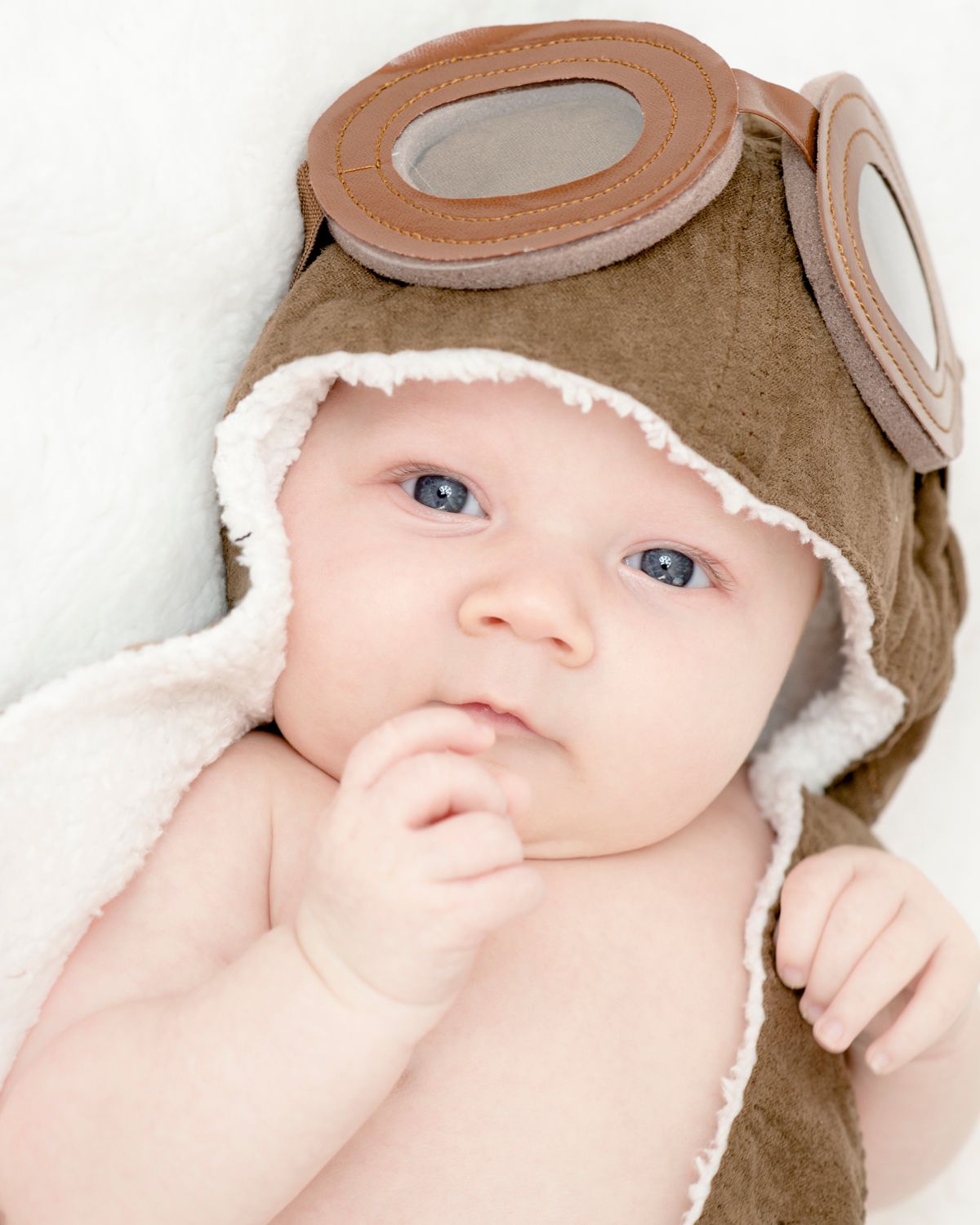 Baby wearing brown aviator hat with white fleece trim looking at camera.