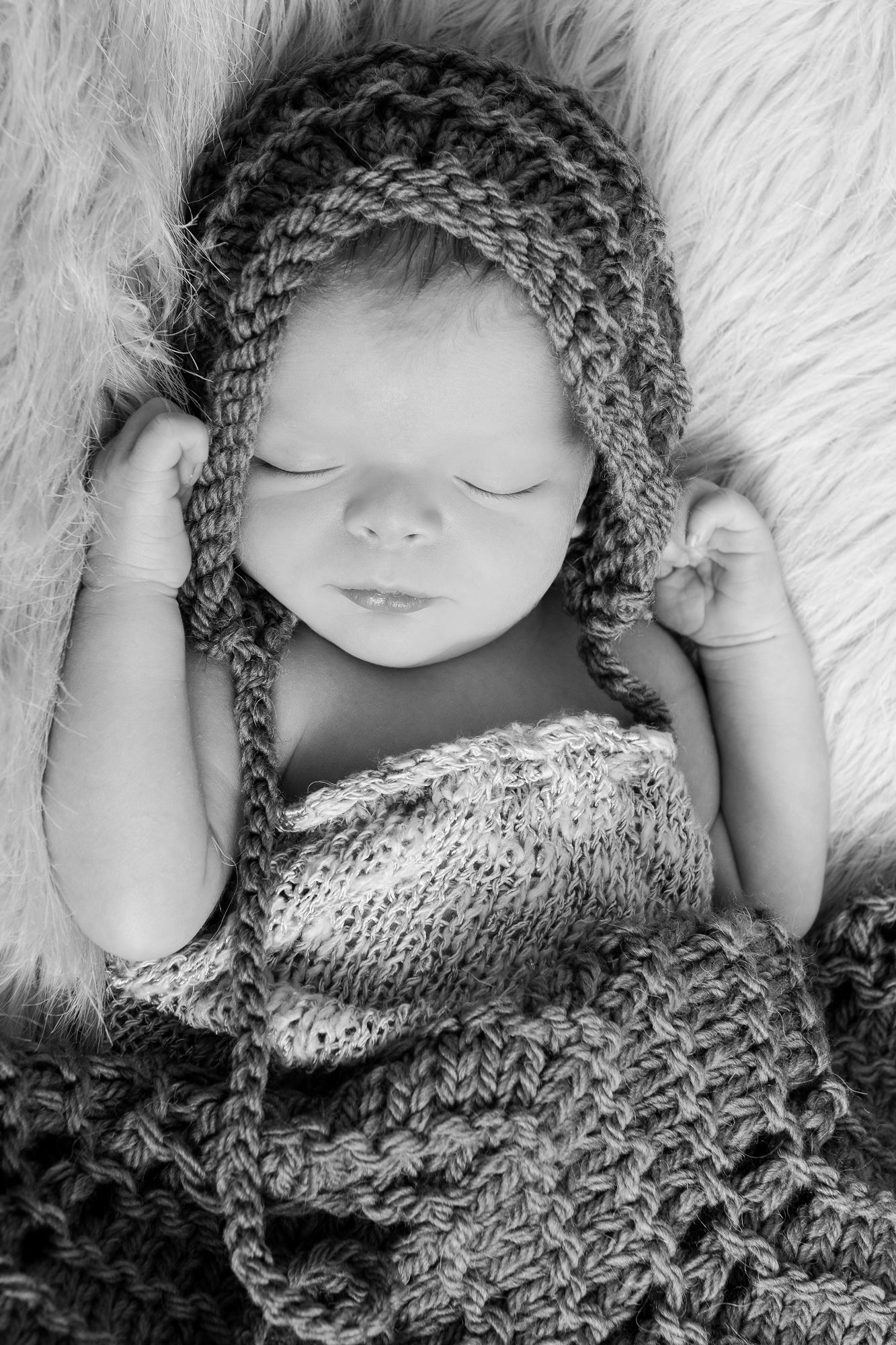 Sleeping newborn wearing knit hat and wrap in black and white portrait.