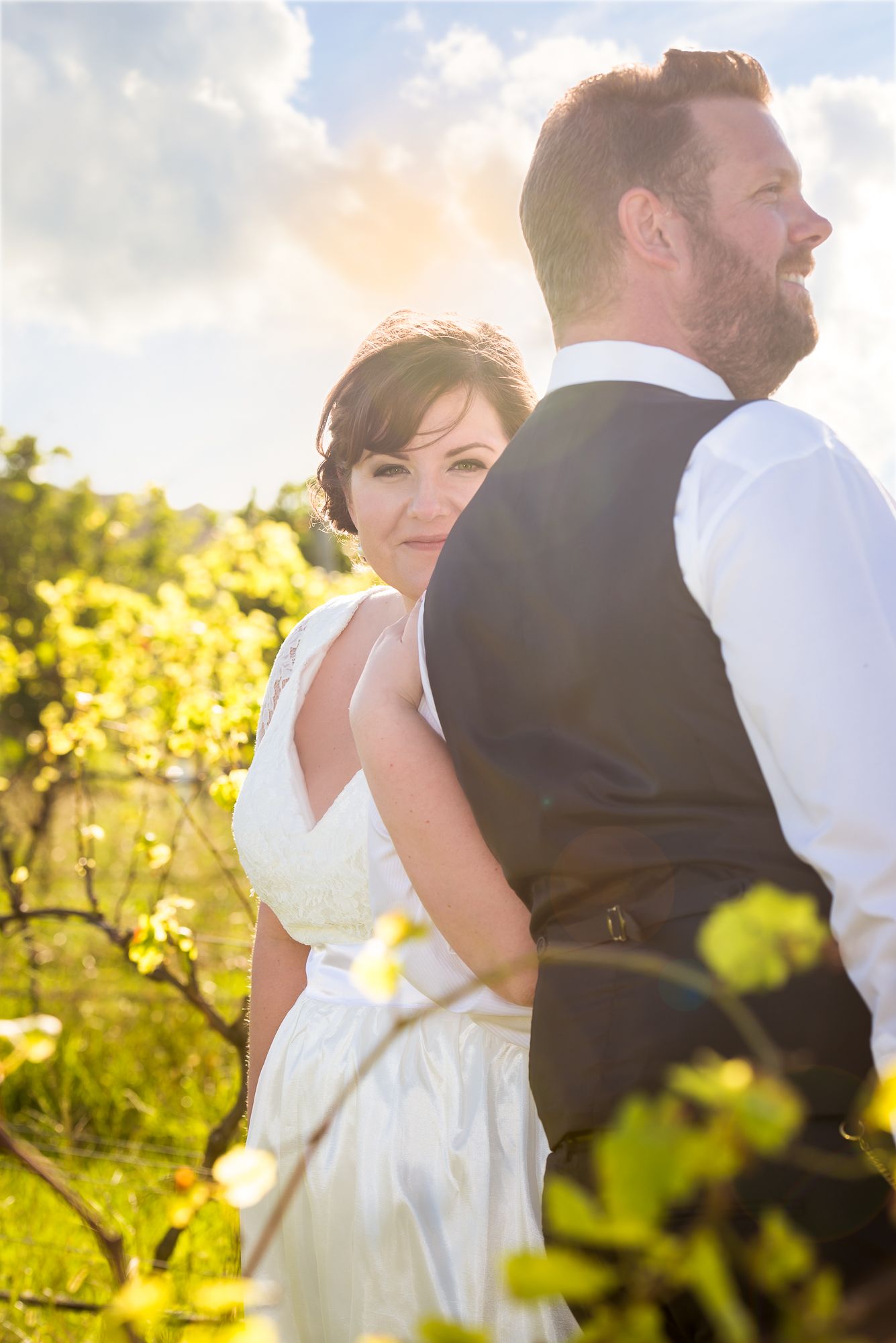 Sunlit wedding portrait session among vineyard rows at golden hour.