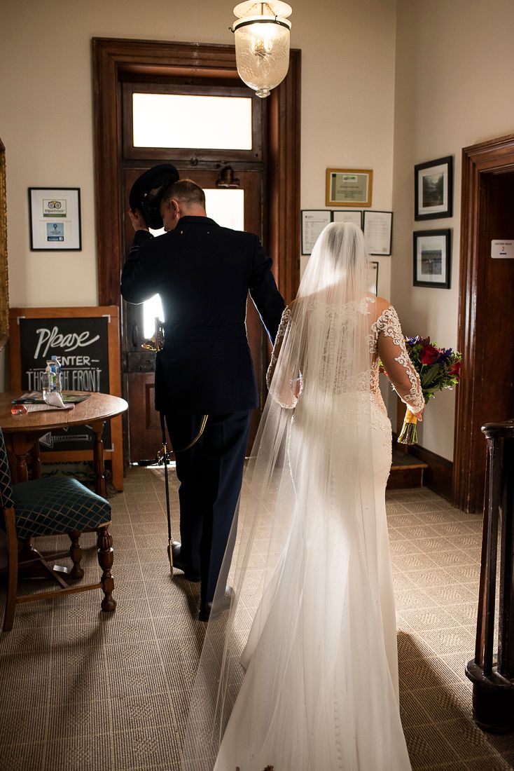 Wedding couple walks through elegant indoor venue with wooden trim and hanging light fixtures.