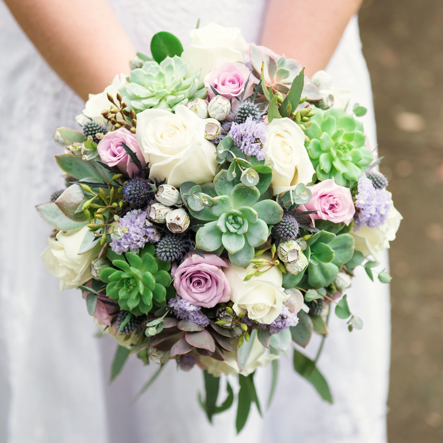 A romantic wedding bouquet featuring white roses, purple flowers, and green succulents.