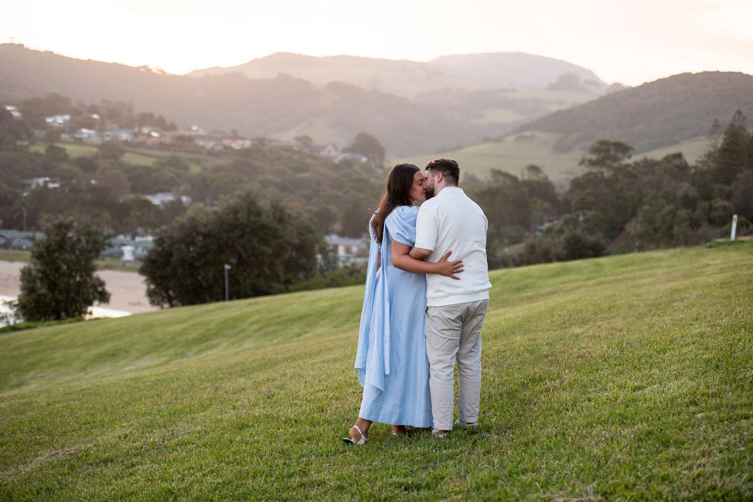 Couple embraces on a hilltop overlooking a scenic mountain valley at sunset.