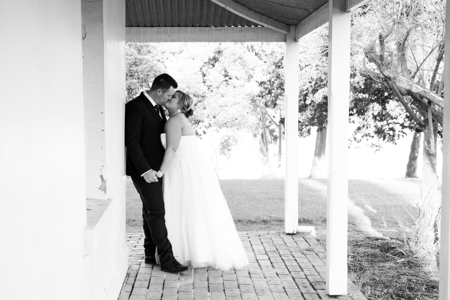 A romantic black and white wedding moment captured on a charming covered porch with white pillars.
