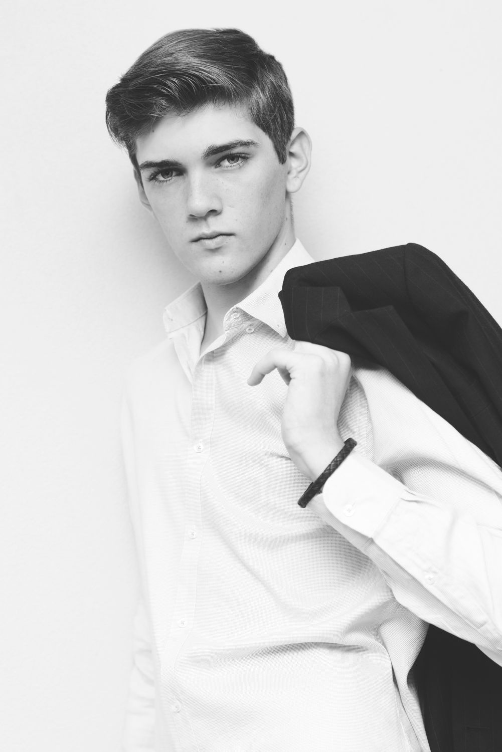 Black and white fashion portrait of a model in formal attire with jacket over shoulder.