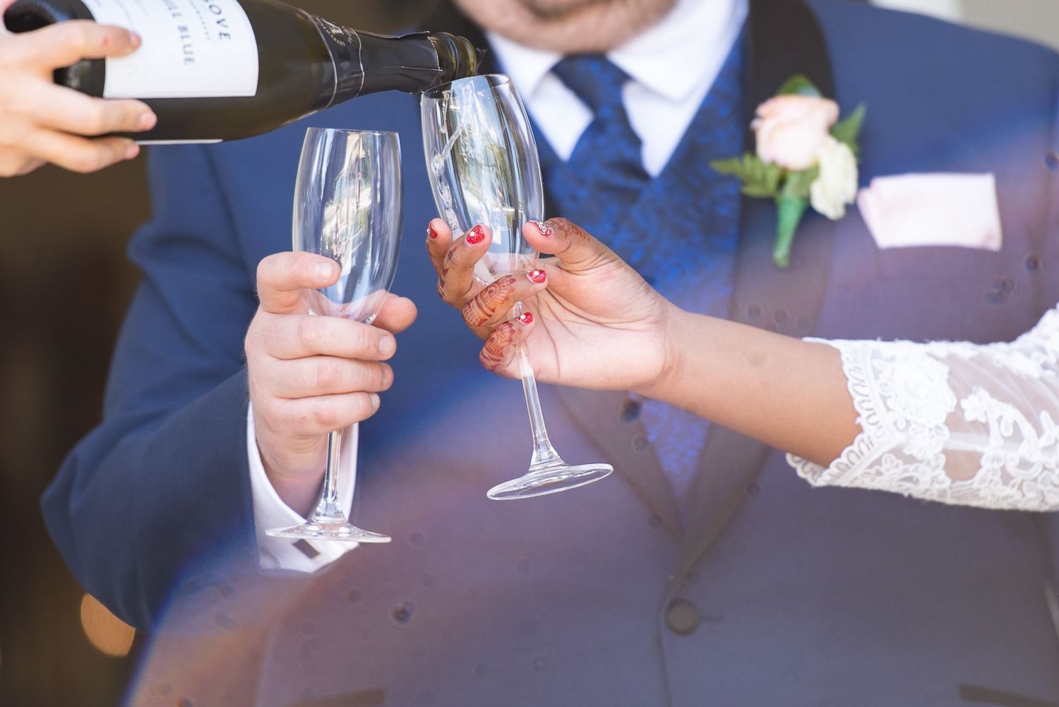 Champagne being poured into elegant flutes during a wedding toast with lace sleeve and navy suit visible.