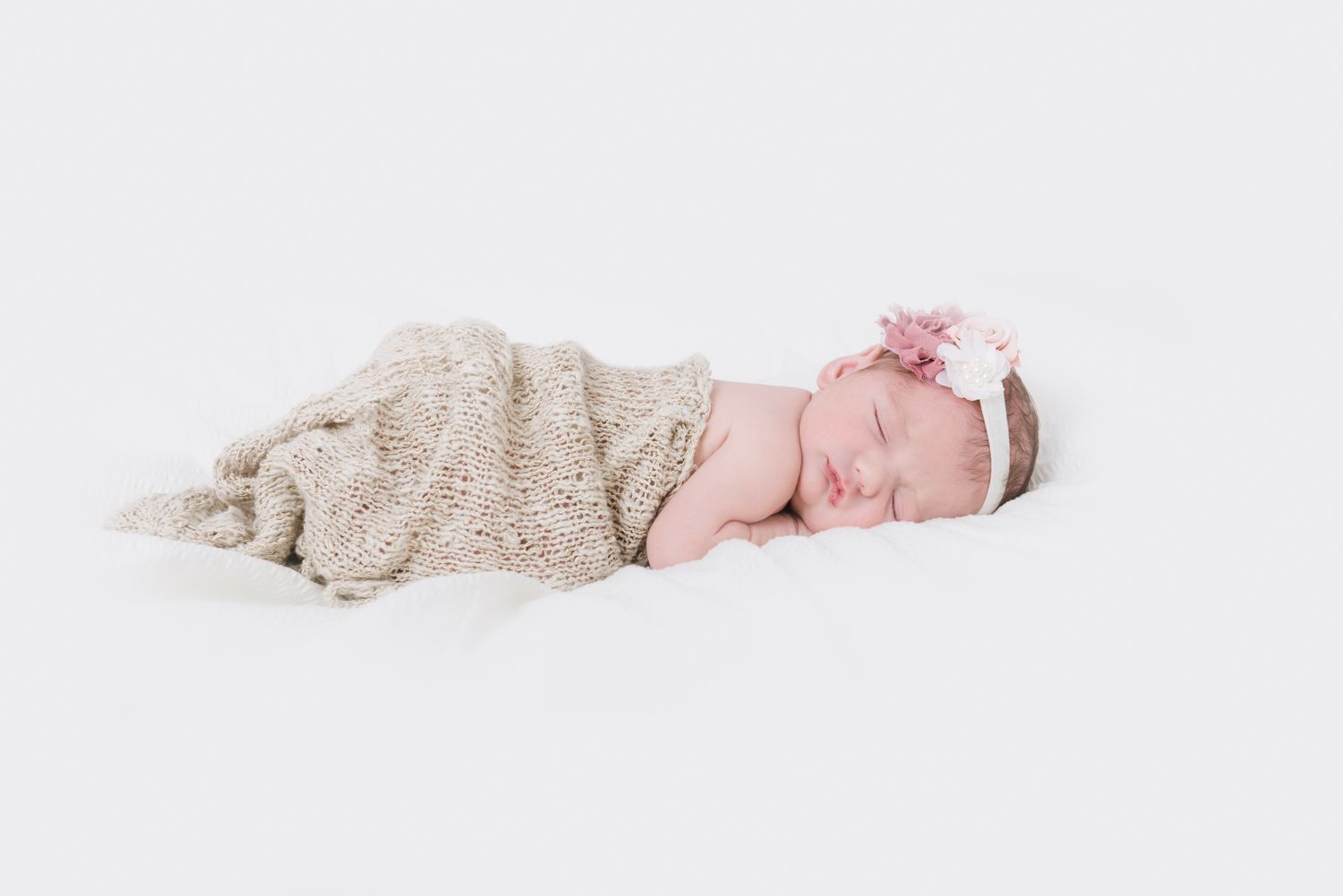 Sleeping baby wrapped in beige blanket on white background.