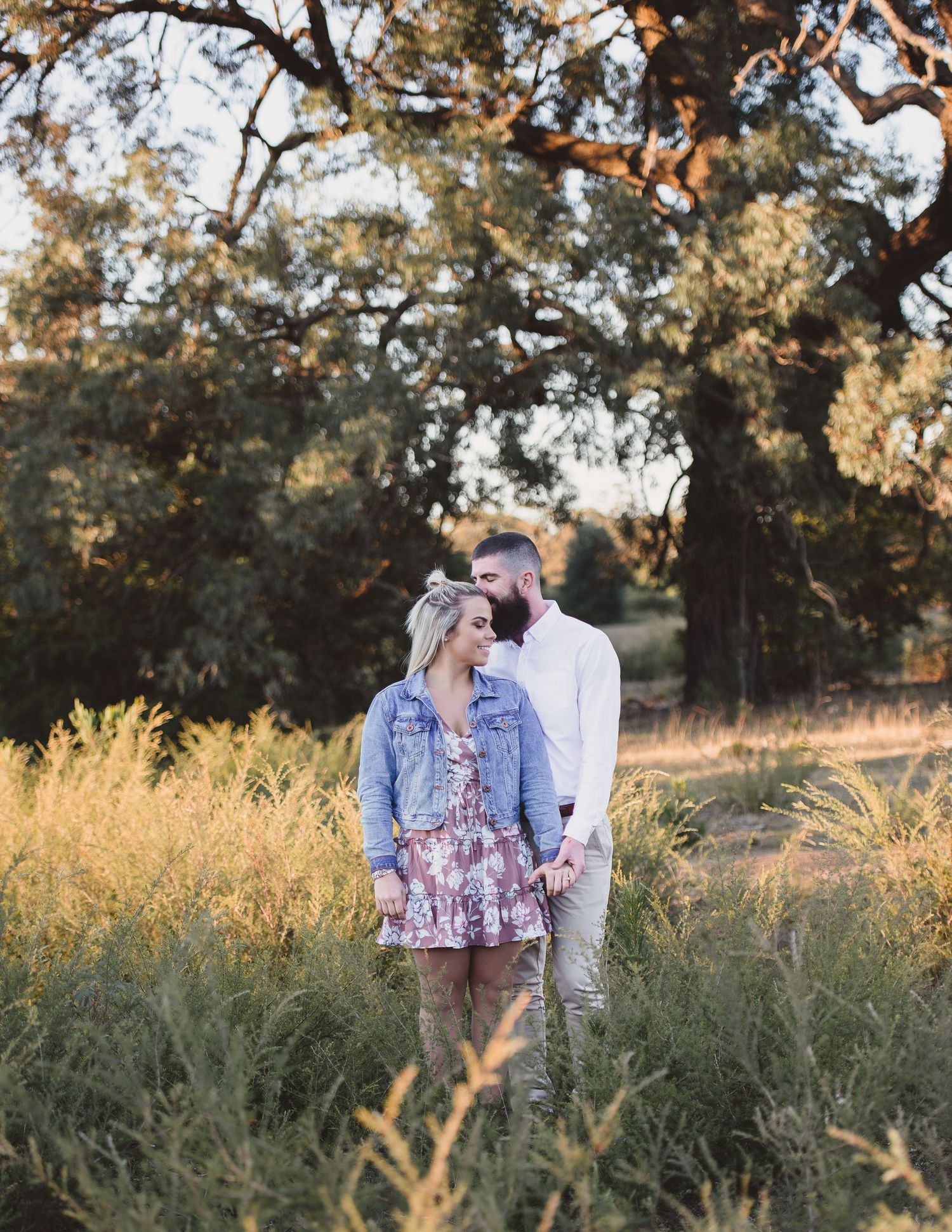 Couple sharing intimate moments in a sunlit field with natural foliage.