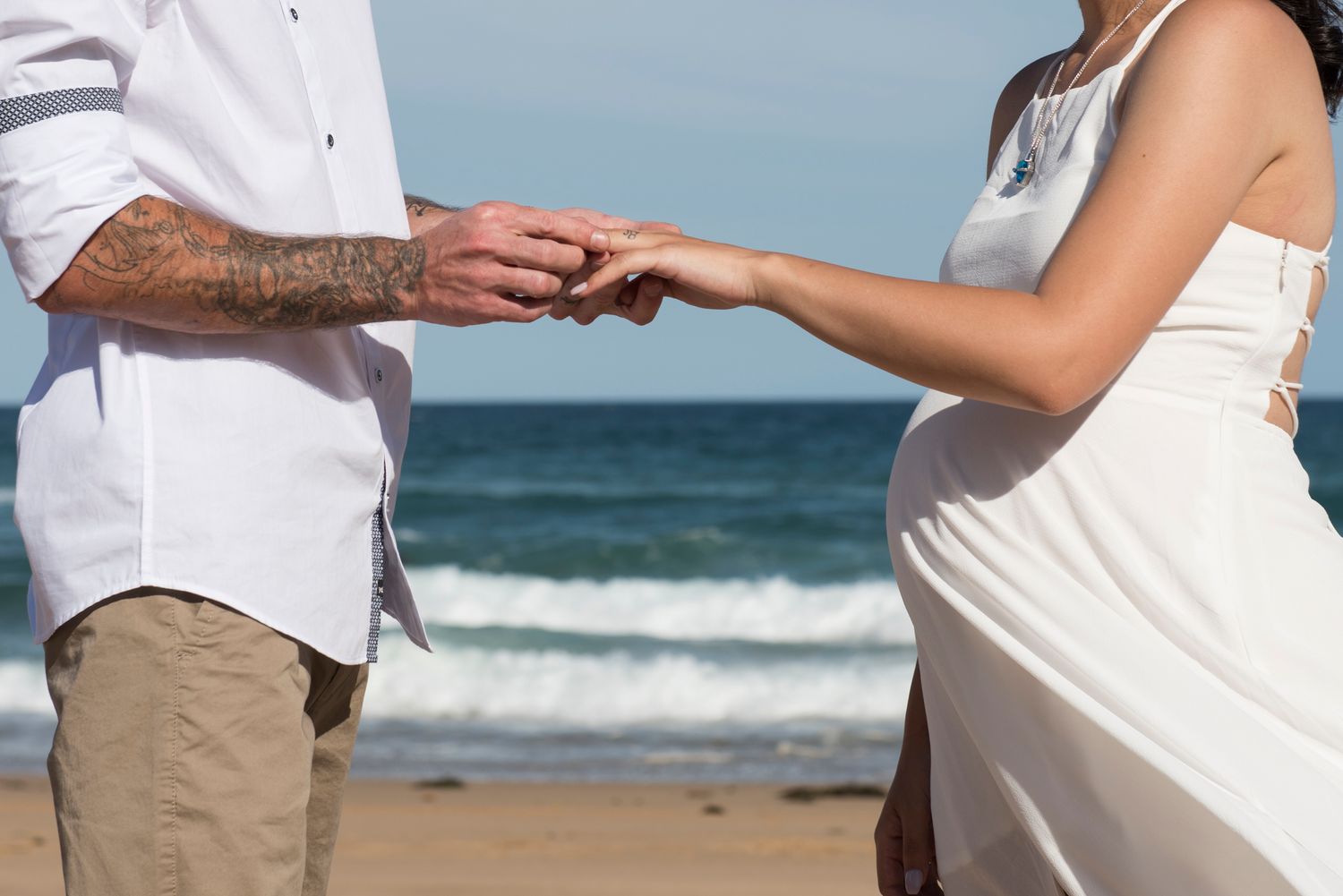 Beach wedding ceremony with couple exchanging rings by the ocean.