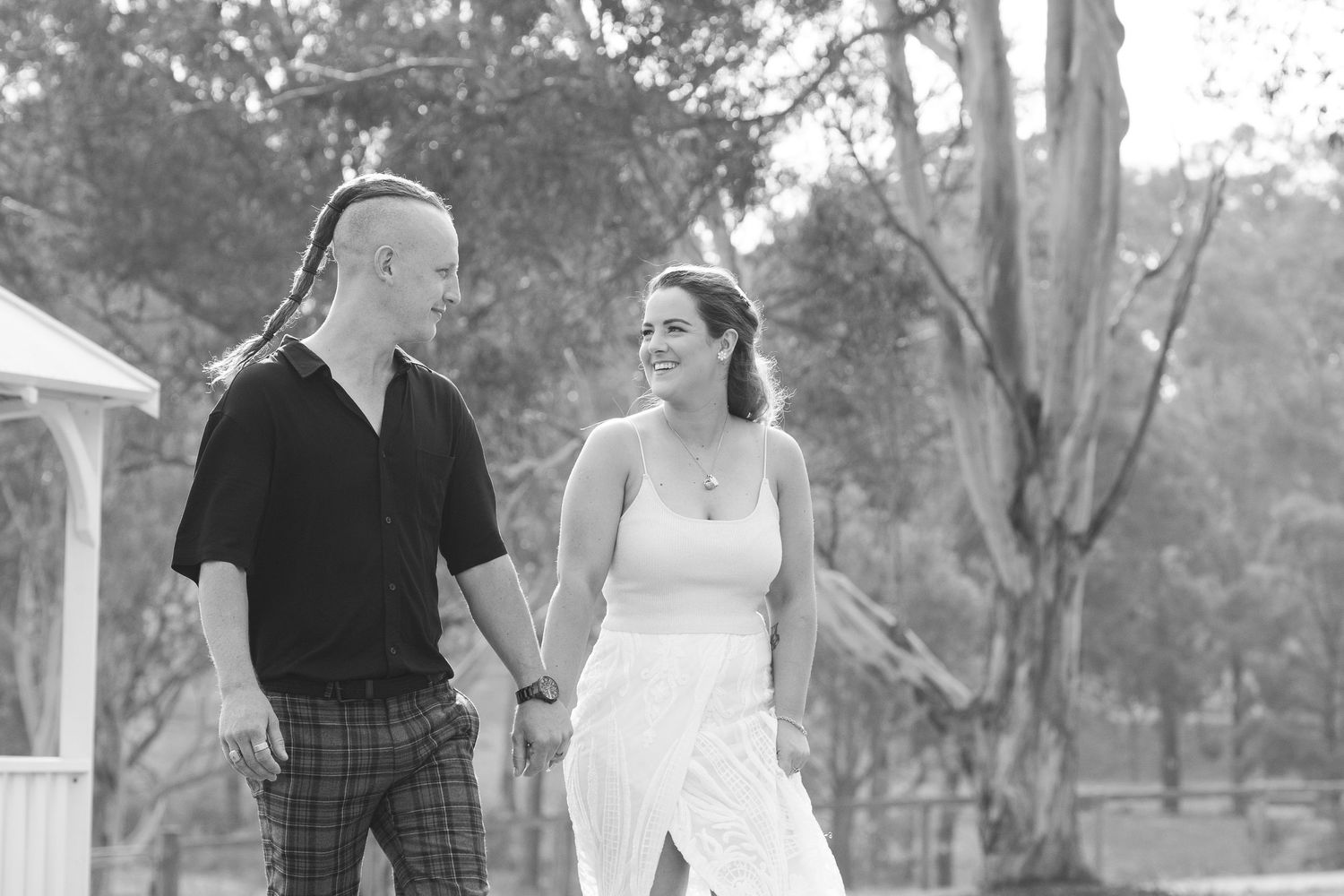 Bride and groom holding hands and smiling at each other while walking outdoors in a black and white photo.