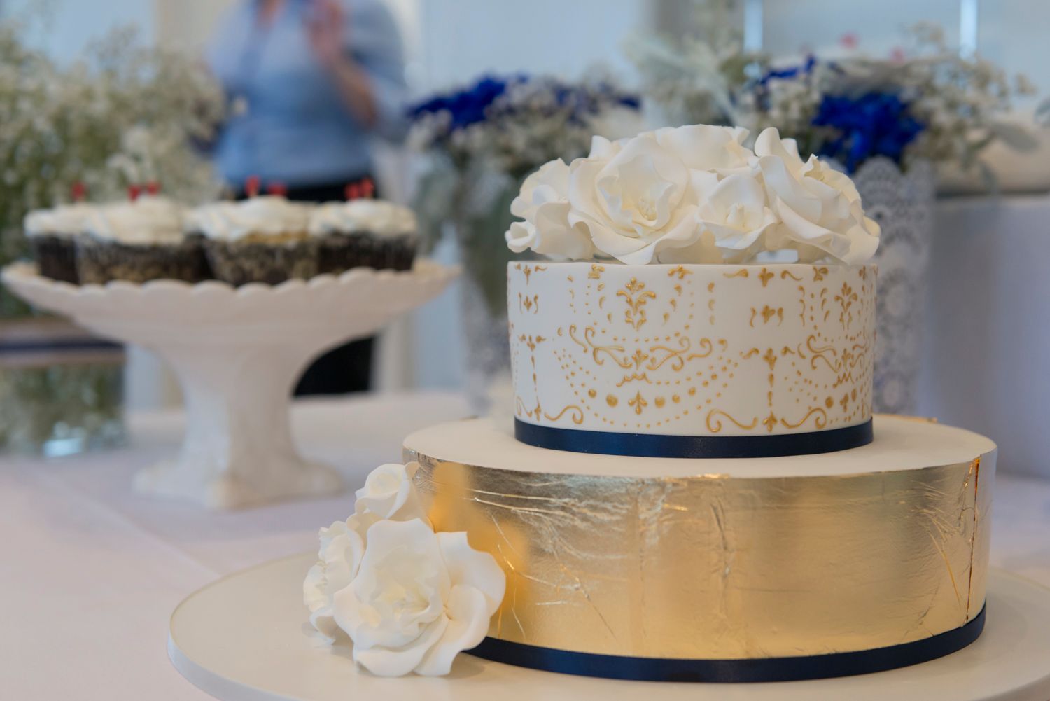 White wedding cake with navy blue ribbon trim and delicate floral decorations displayed on a table.