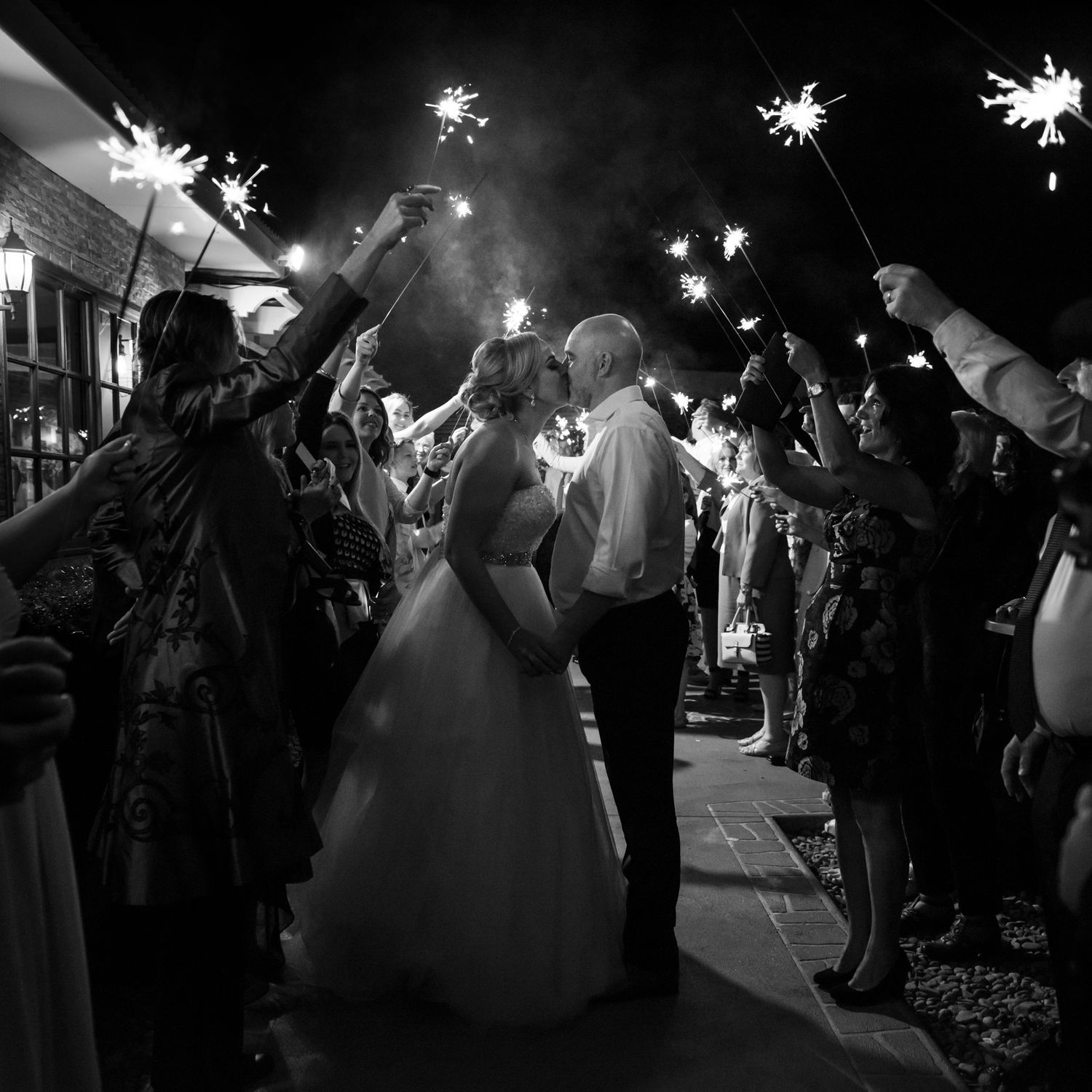 Wedding guests hold sparklers creating a magical night time send-off tunnel for the newlyweds.