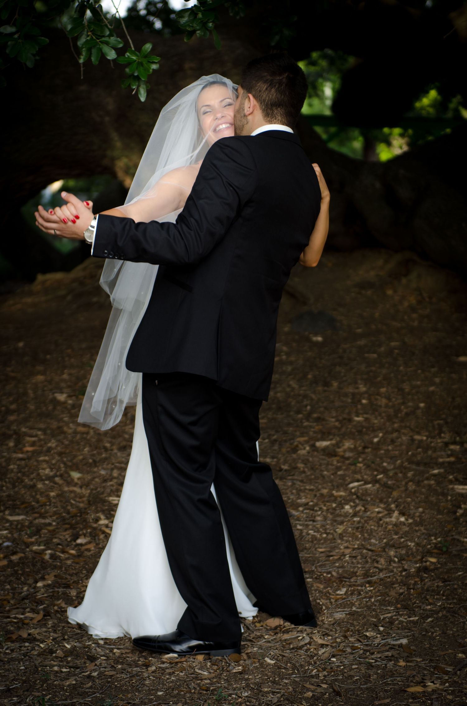 Romantic first dance sequence between newlyweds on rustic ground under tree canopy.
