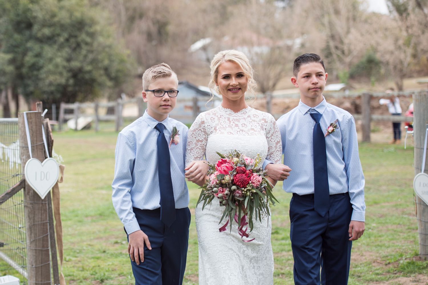 Mum with sons each side, walks through a gate to wedding ceremony.
