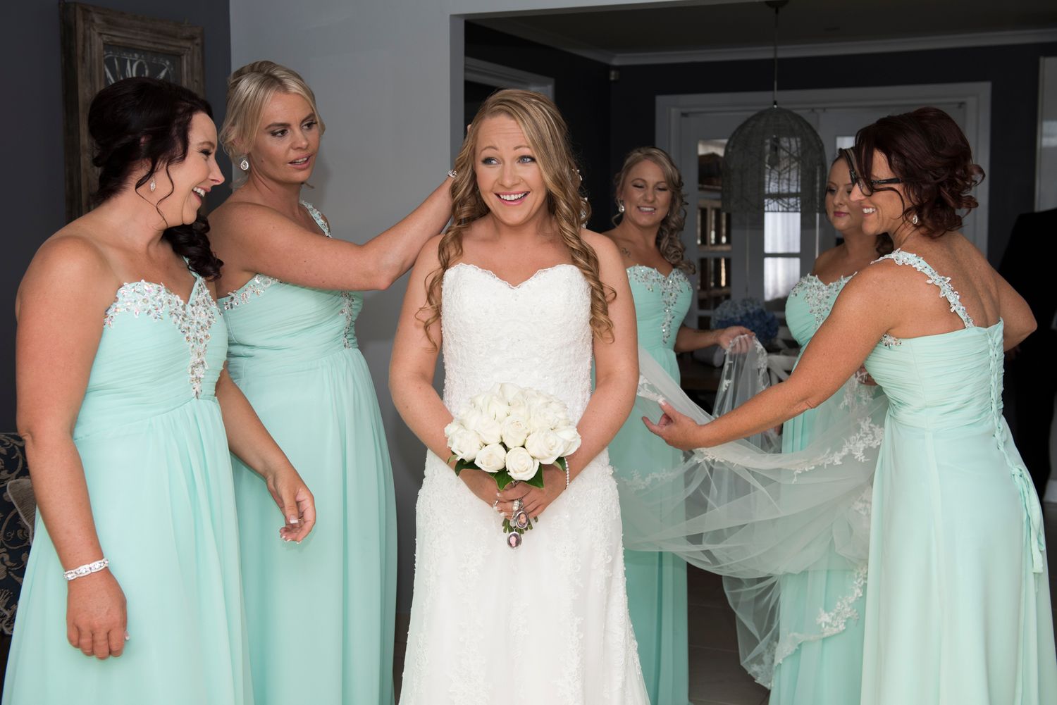 Bridesmaids in mint green dresses with bride pose together as bride is getting ready.