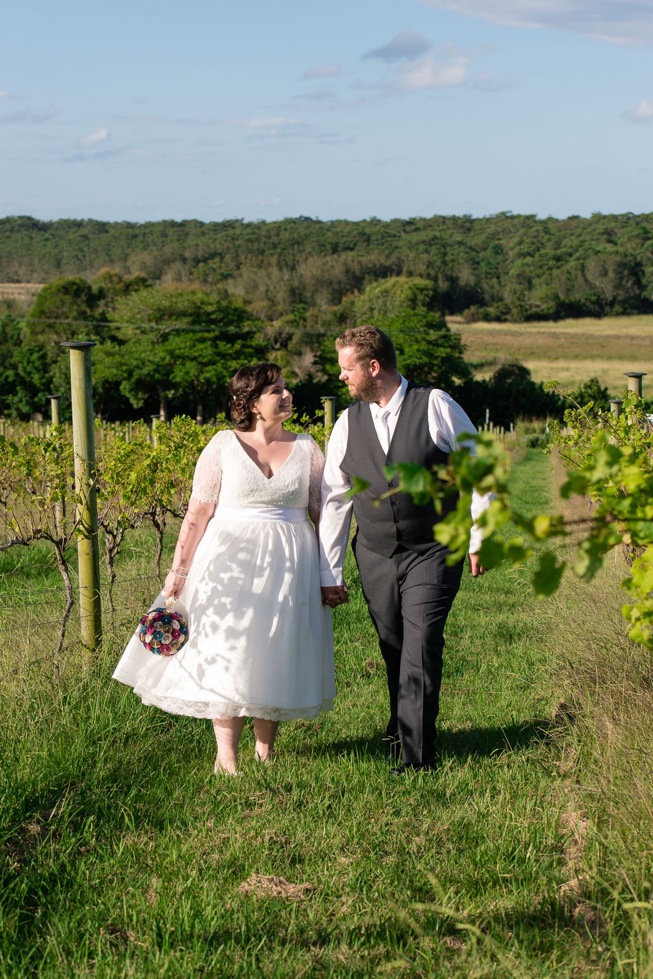 Newlyweds walking through a scenic vineyard on their wedding day.