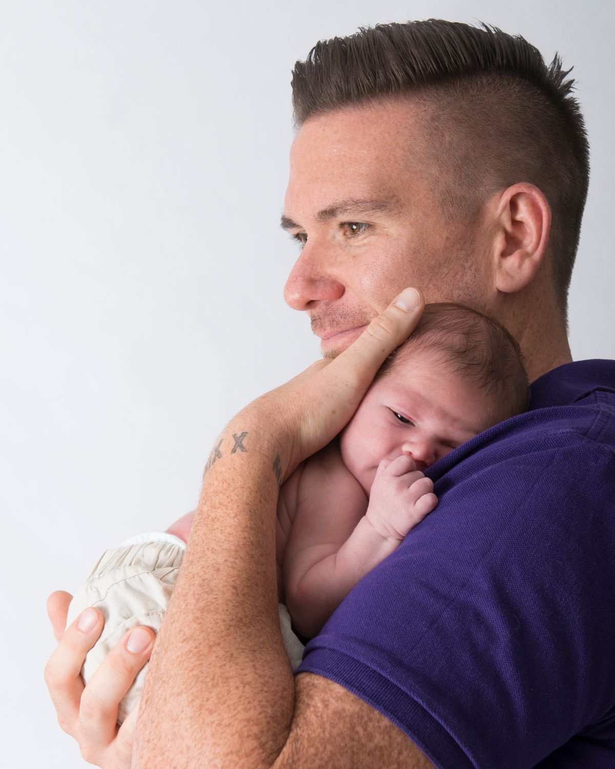Parent in purple shirt holding sleeping newborn against shoulder.