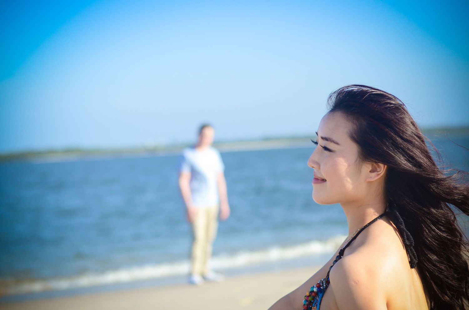 Romantic couple on a scenic beach with blue skies and ocean waves in background.