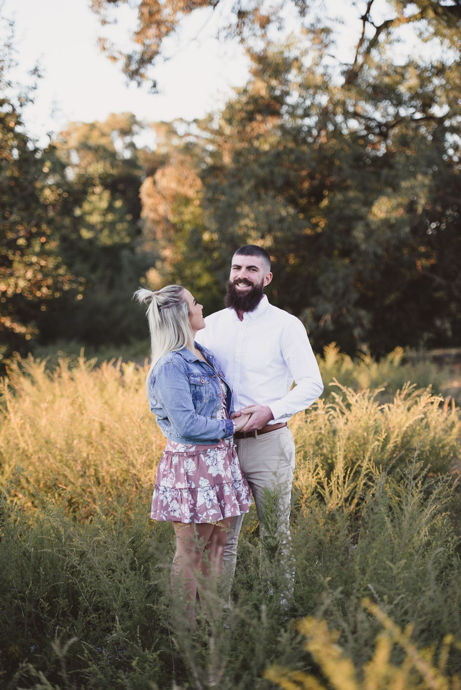 Romantic photoshoot in a tall grass field during golden hour with trees in background.