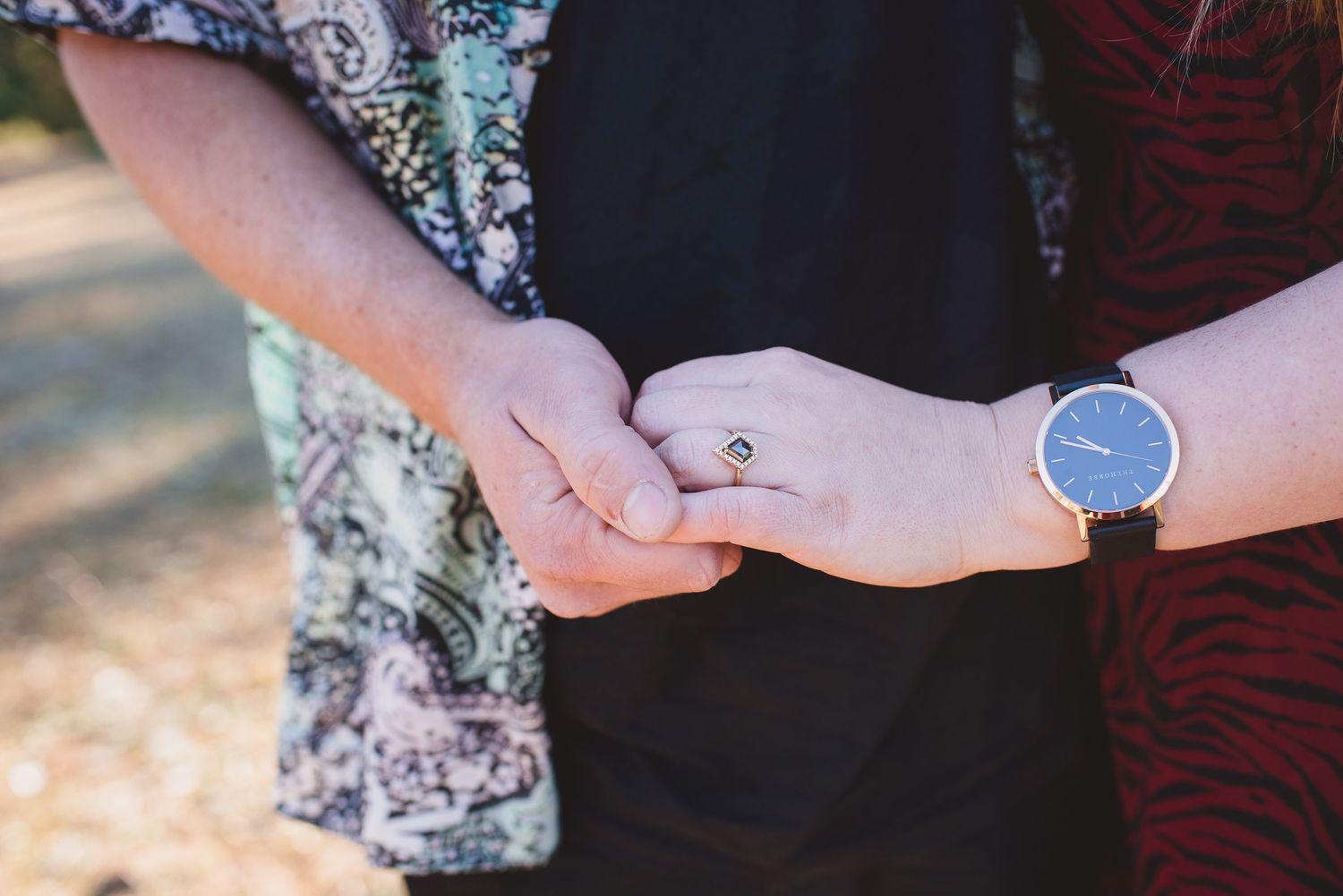 Close up of hands holding each other tenderly outdoors.