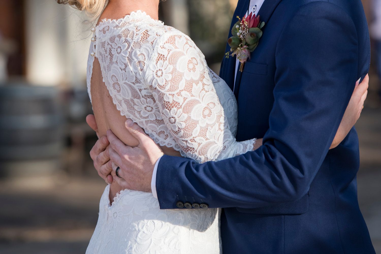 Bride and Groom embrace during an outdoor ceremony, with the bride wearing a white lace dress.