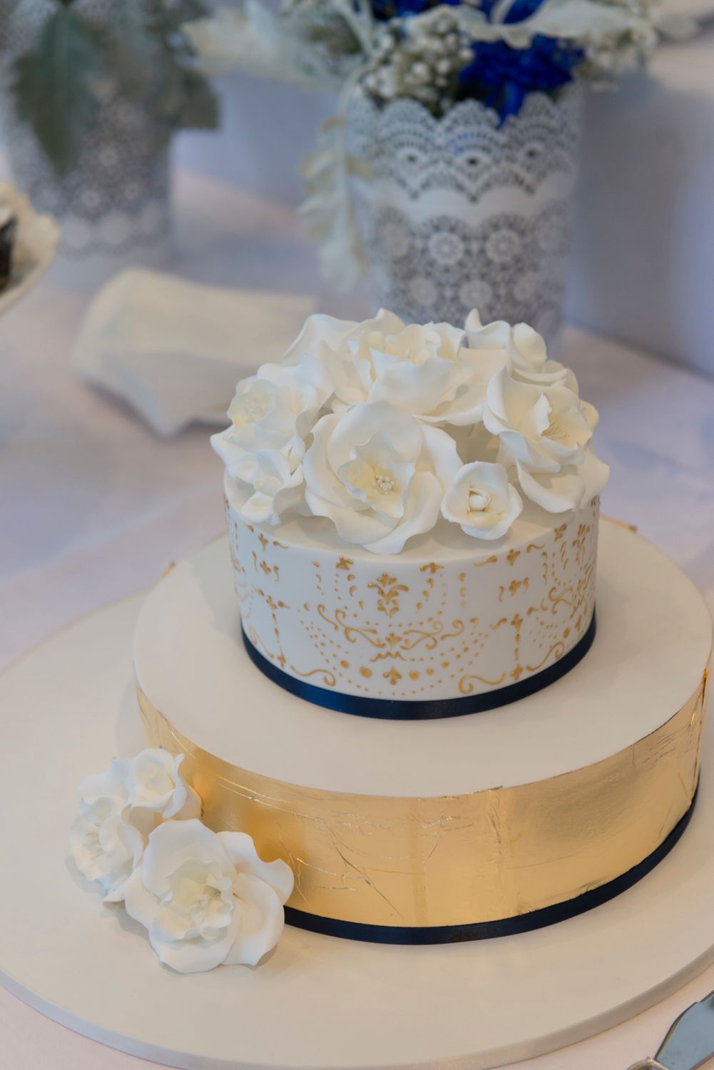 Elegant white wedding cake decorated with delicate sugar flowers and a navy blue ribbon accent on multiple tiers.
