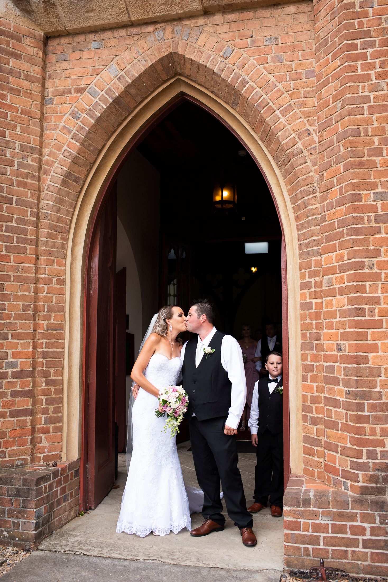 A wedding couple shares a romantic moment under a series of brick archways at a historic venue.